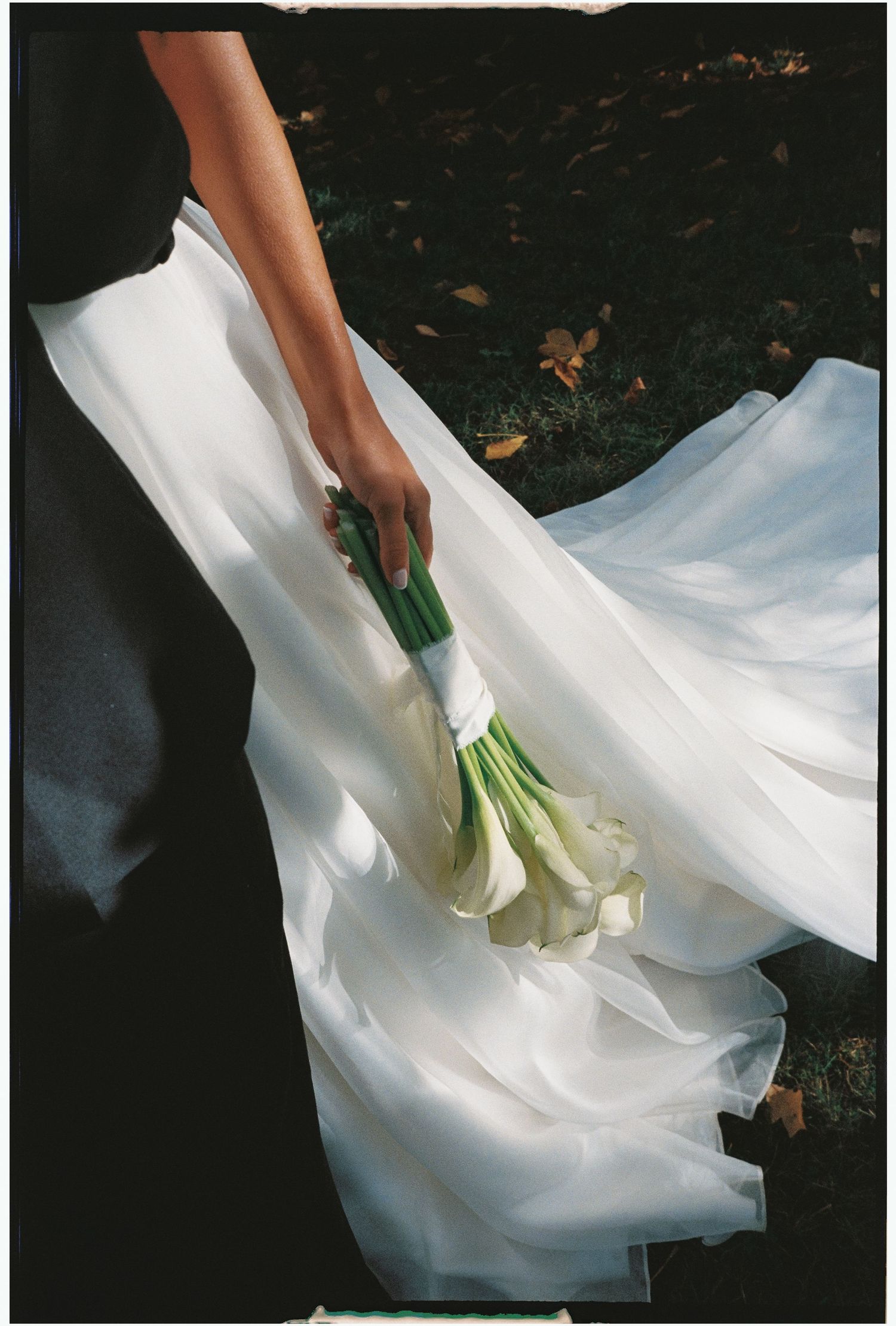 White fabric being arranged on a dark surface with hands holding green foliage.