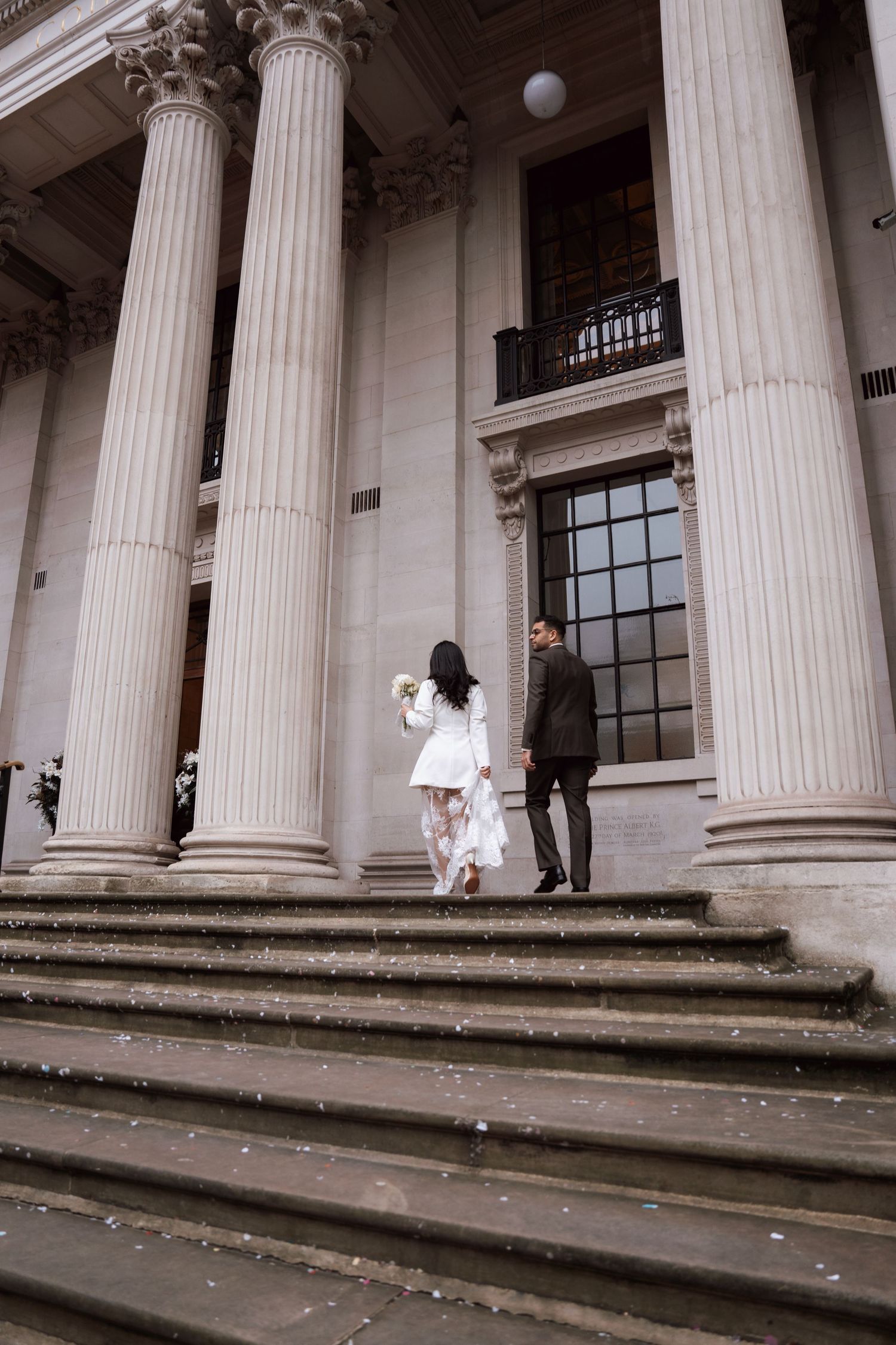 Elegant neoclassical building entrance with white columns and steps where a couple poses for wedding photos.