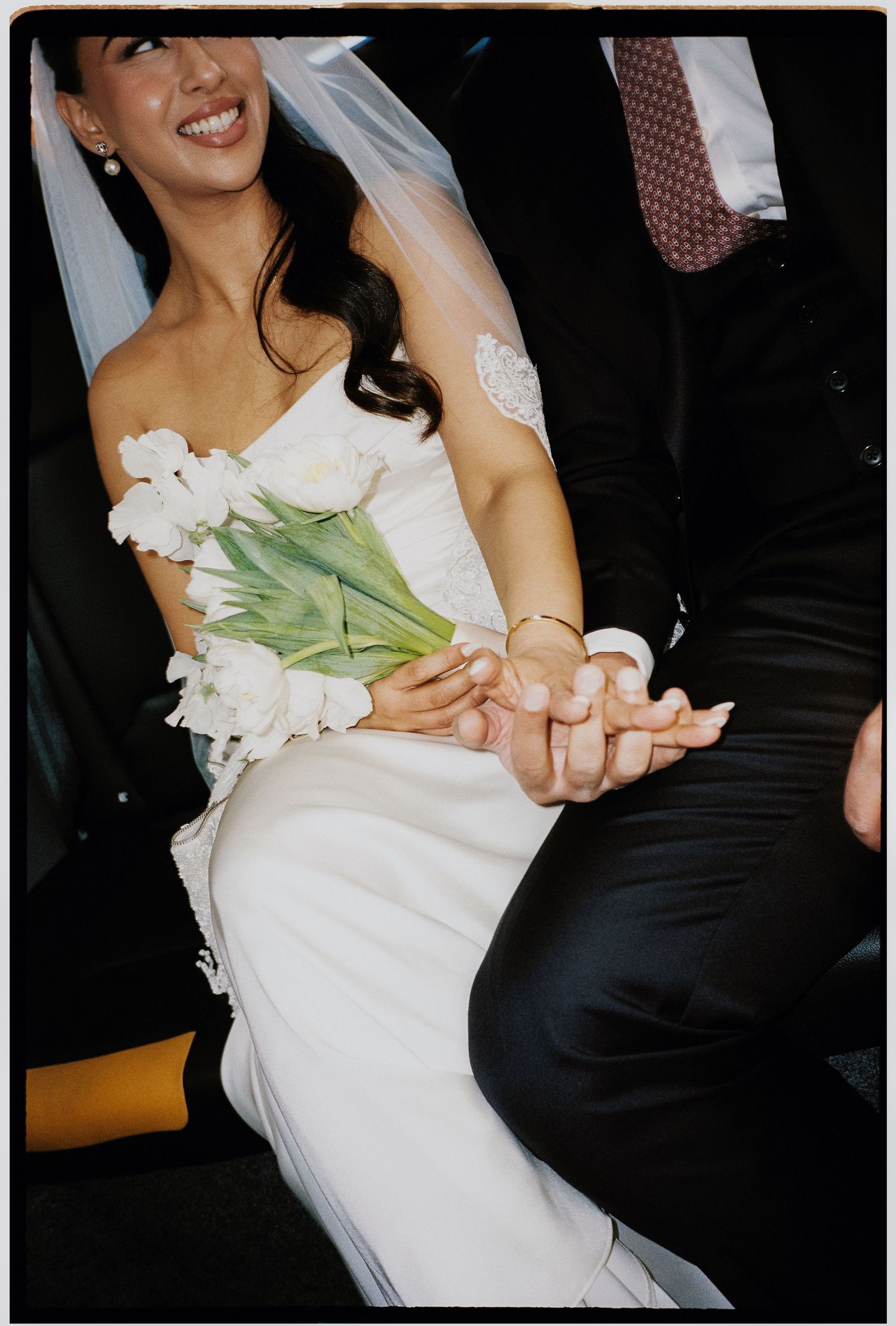 A bride in a white wedding dress holds tulips while seated at a reception table during a celebration.