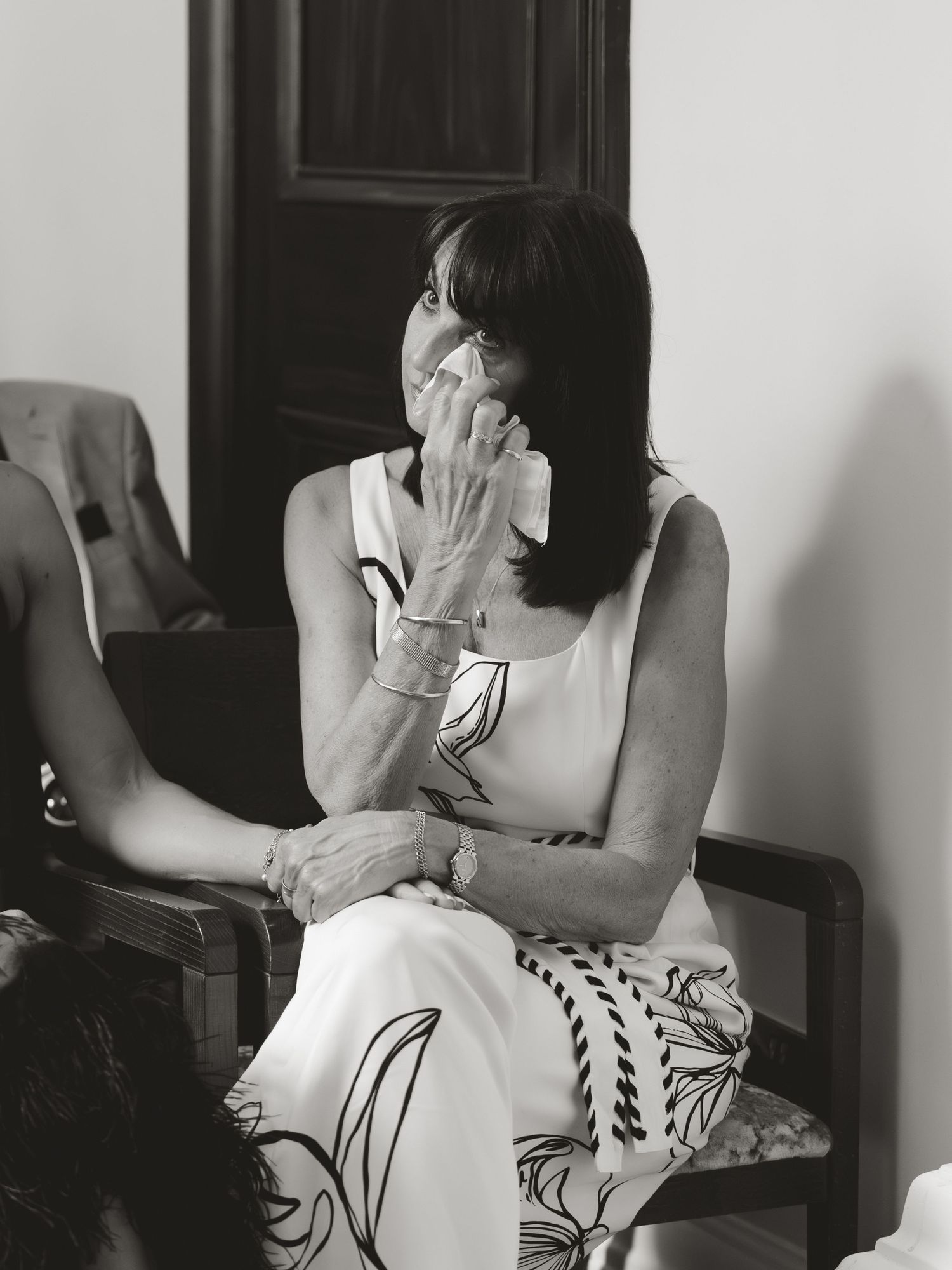 Black and white photo of a woman in floral dress wiping tears with tissue while seated at an emotional event.