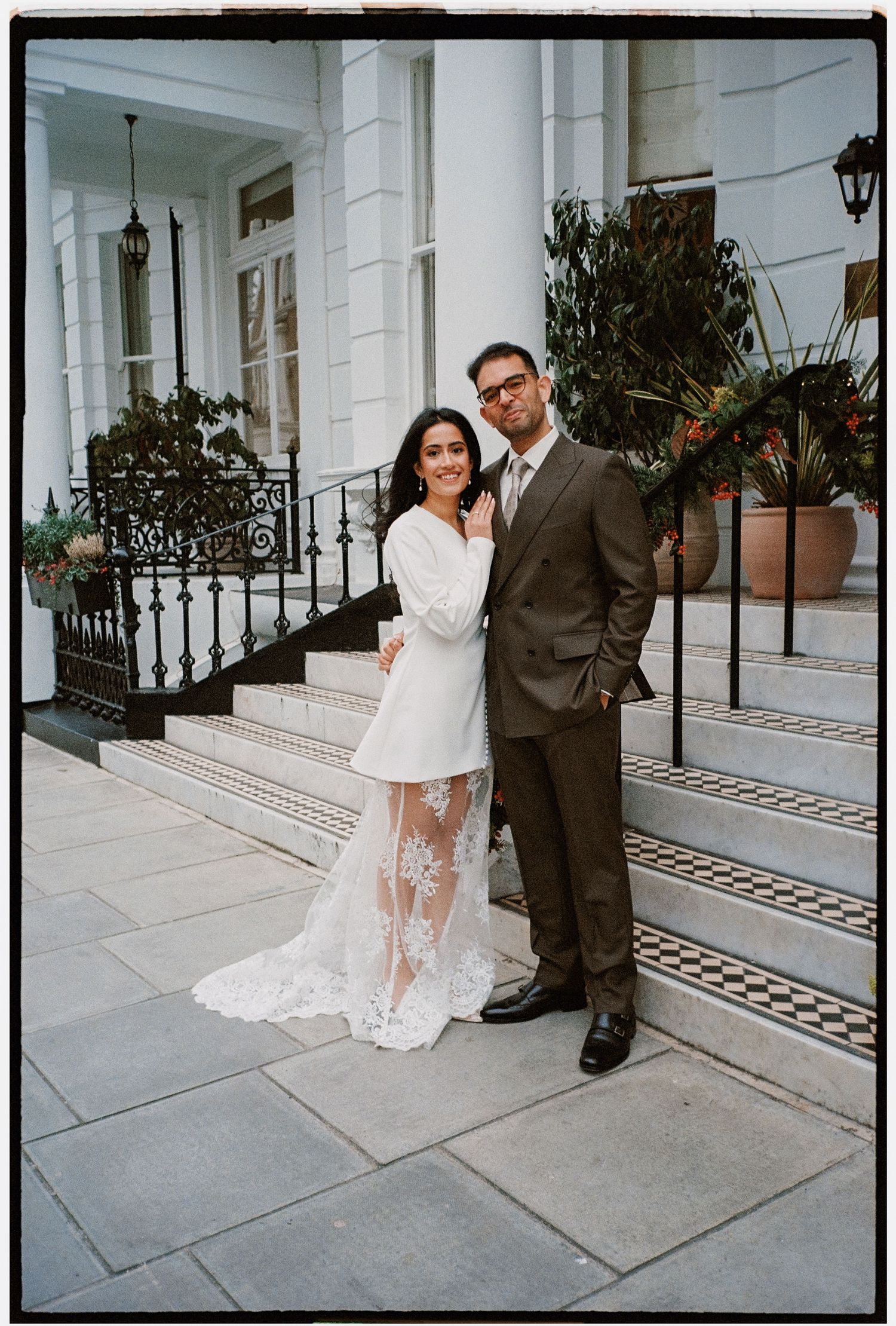 A newlywed couple poses on elegant stone steps in front of a white columned building.