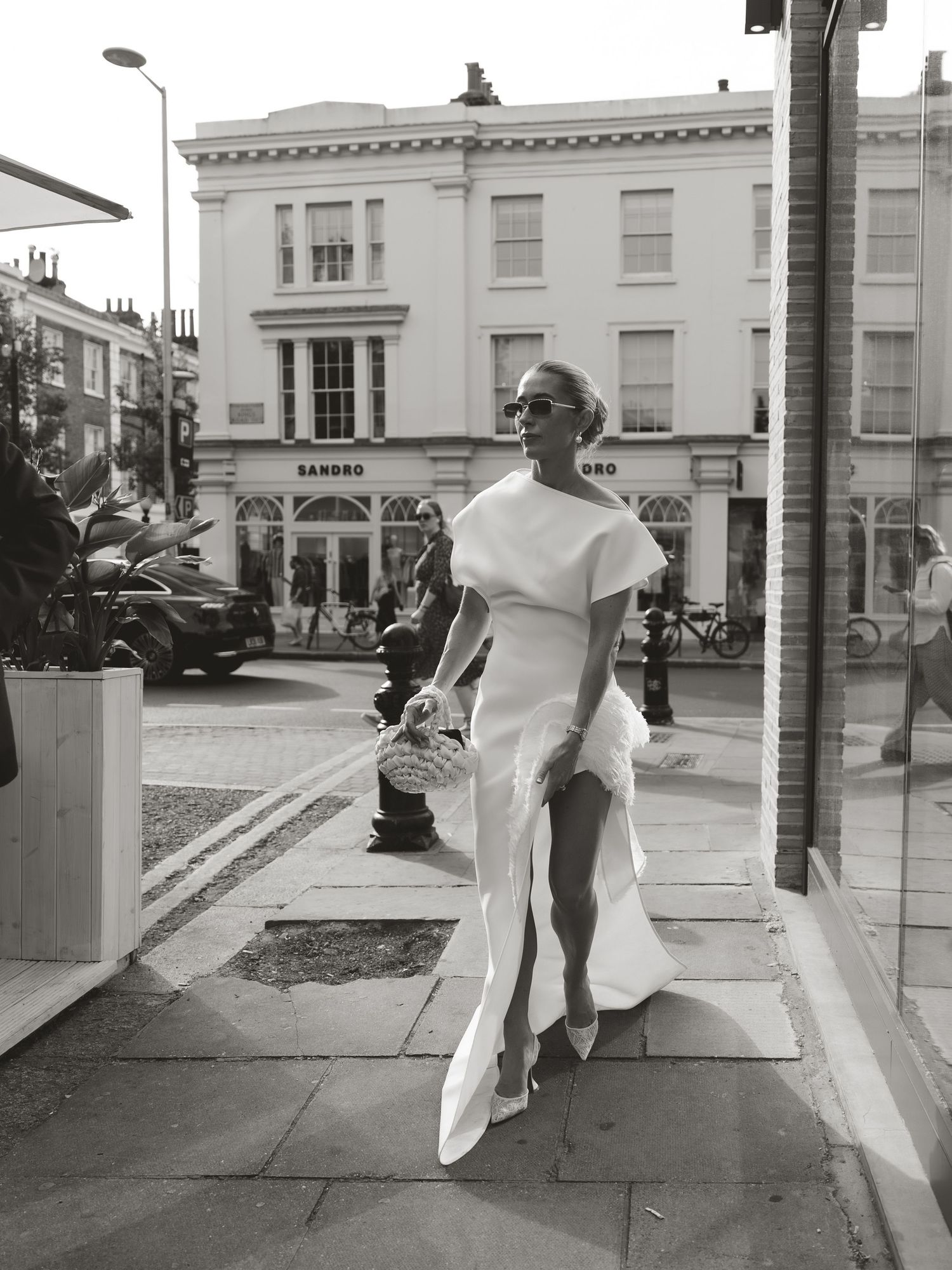 Woman in white dress walking on London street in black and white photo, Sandro store in background.