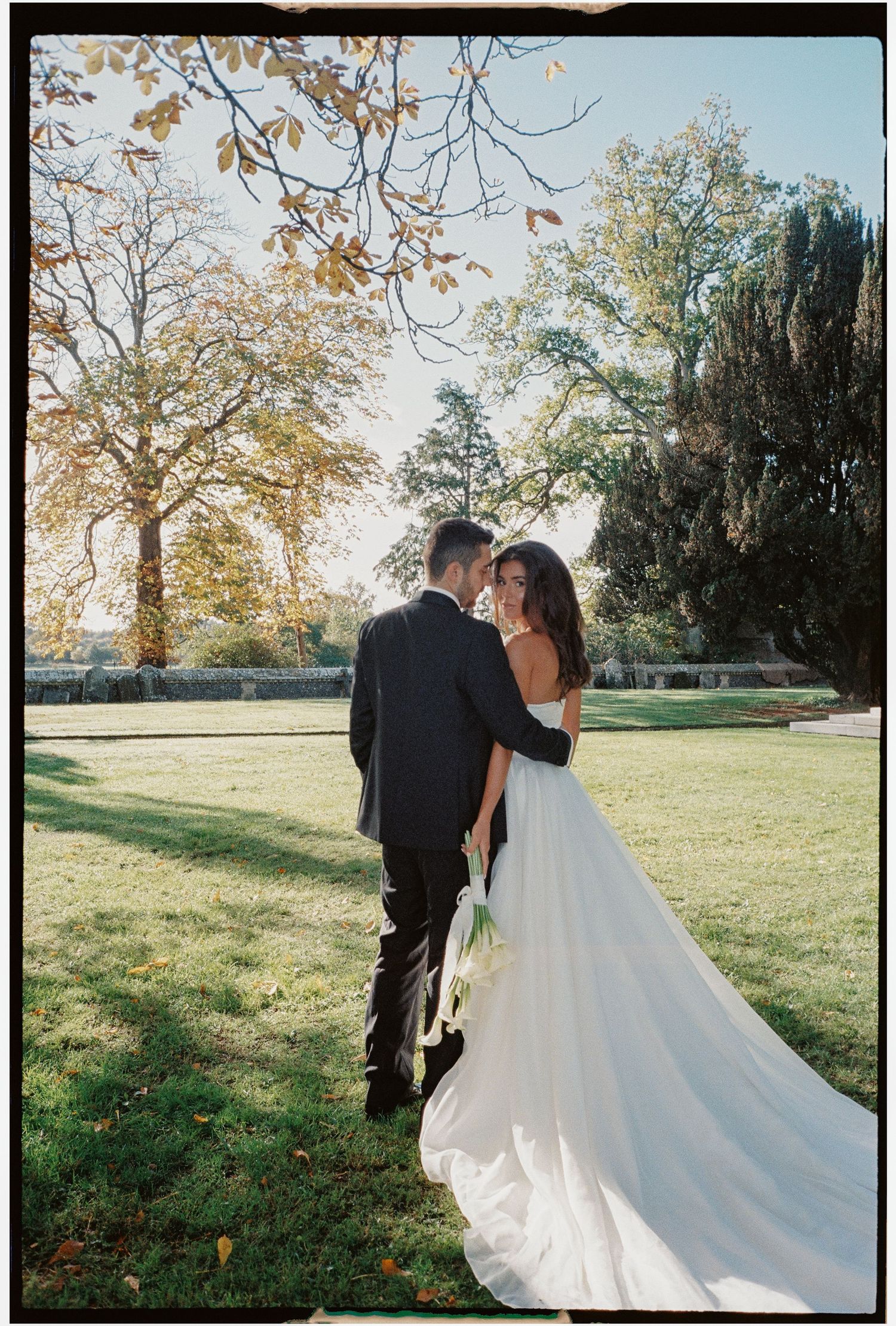 Couple in wedding attire walking through an autumn field.