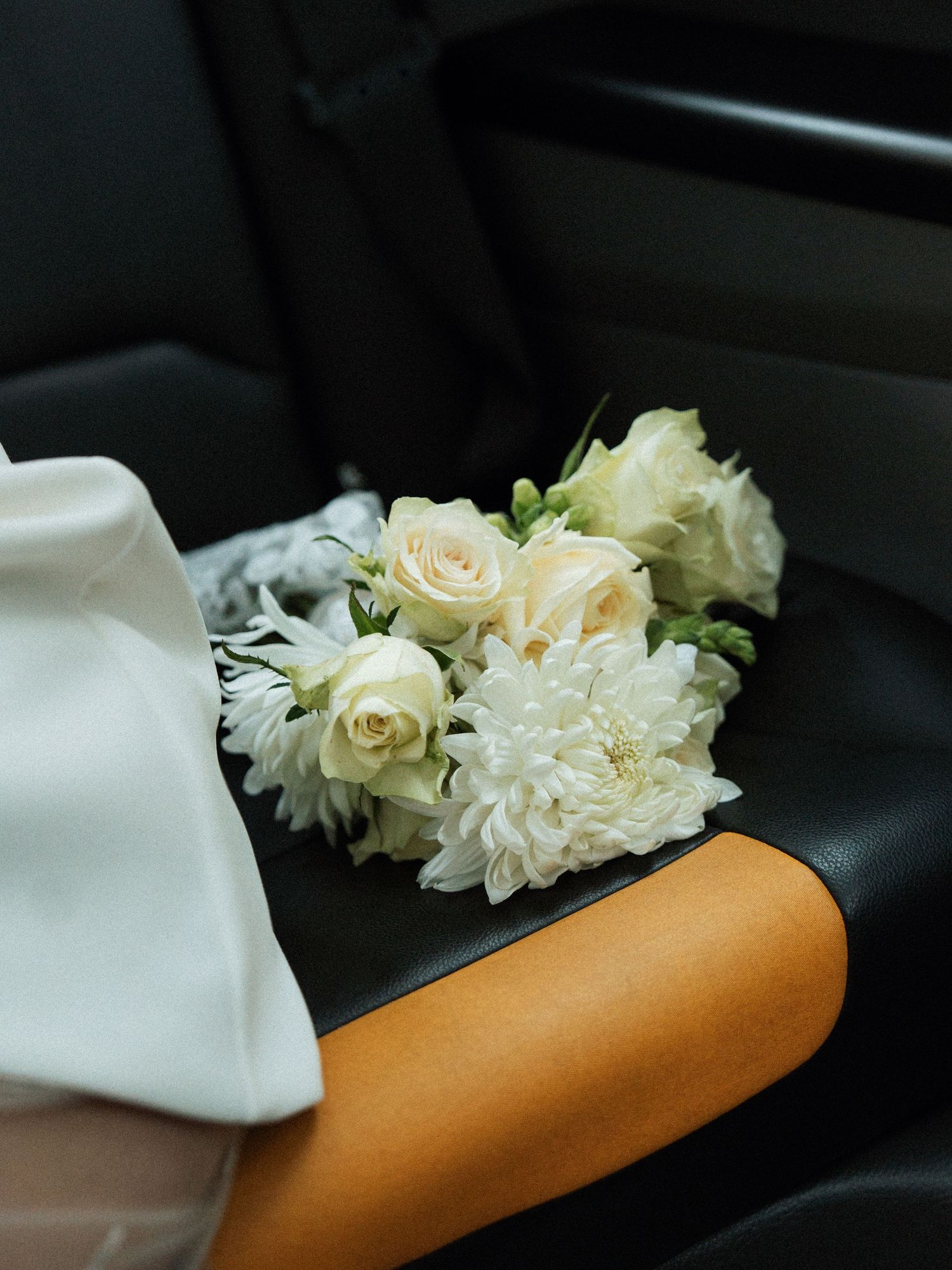 White roses and flowers rest on an orange fabric in a dark interior setting.