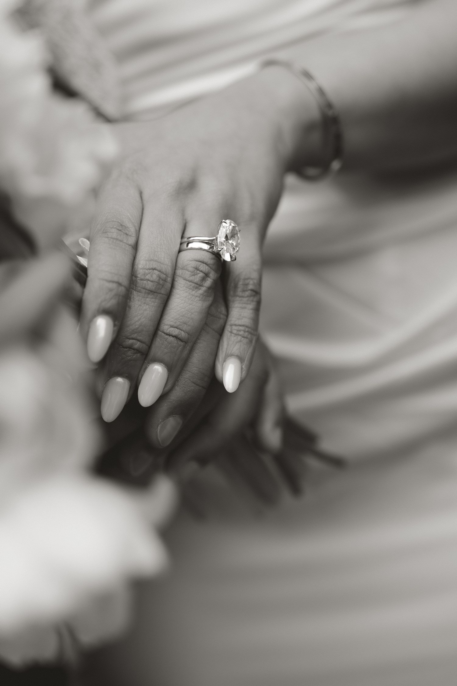 Black and white photo of a bride's hands displaying a diamond engagement ring and wedding band with manicured nails.