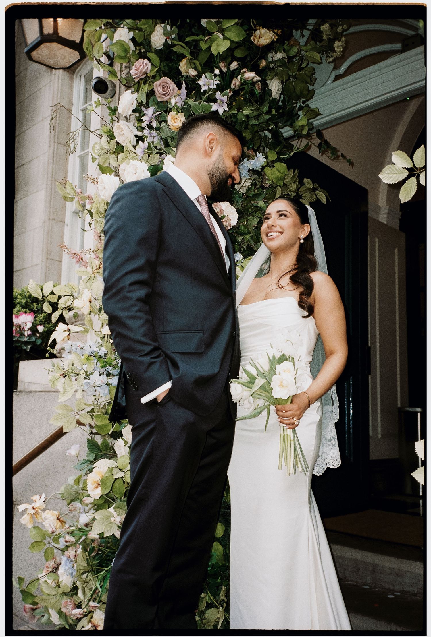 Elegant wedding couple embraces under floral archway in romantic black and white photos.