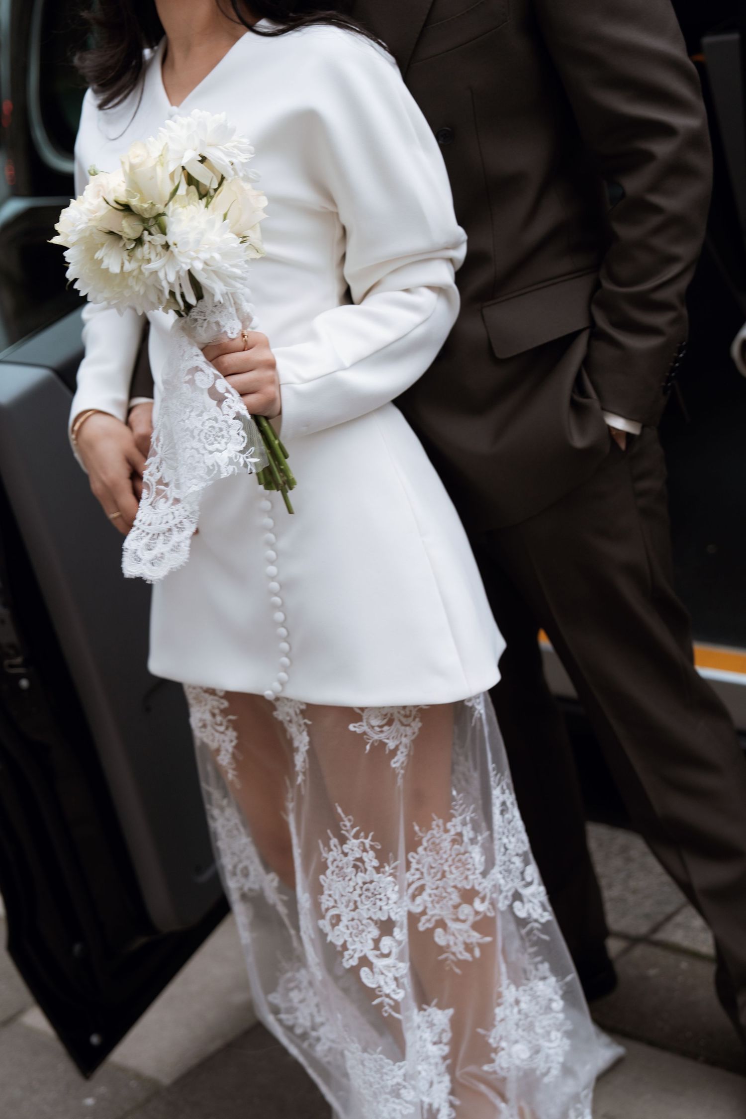 Detail of bride's white lace wedding dress with sheer overlay and floral embellishments.