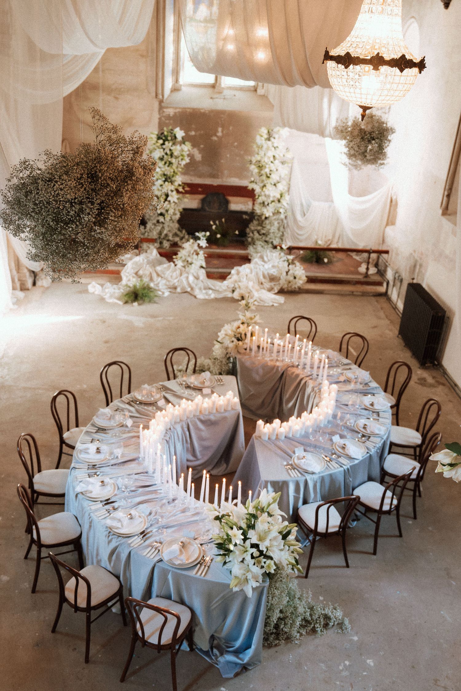 An elegant wedding reception table with blue linens and white floral centerpieces in a rustic venue.
