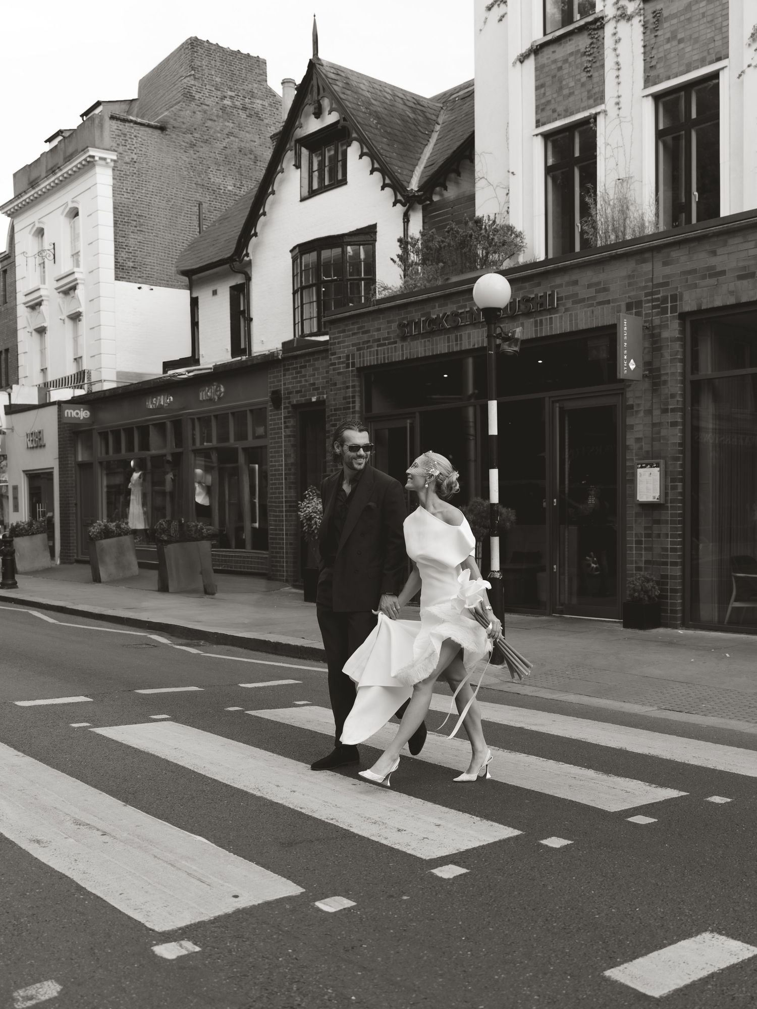 Black and white photo of a bride and groom crossing a zebra crossing on a city street.