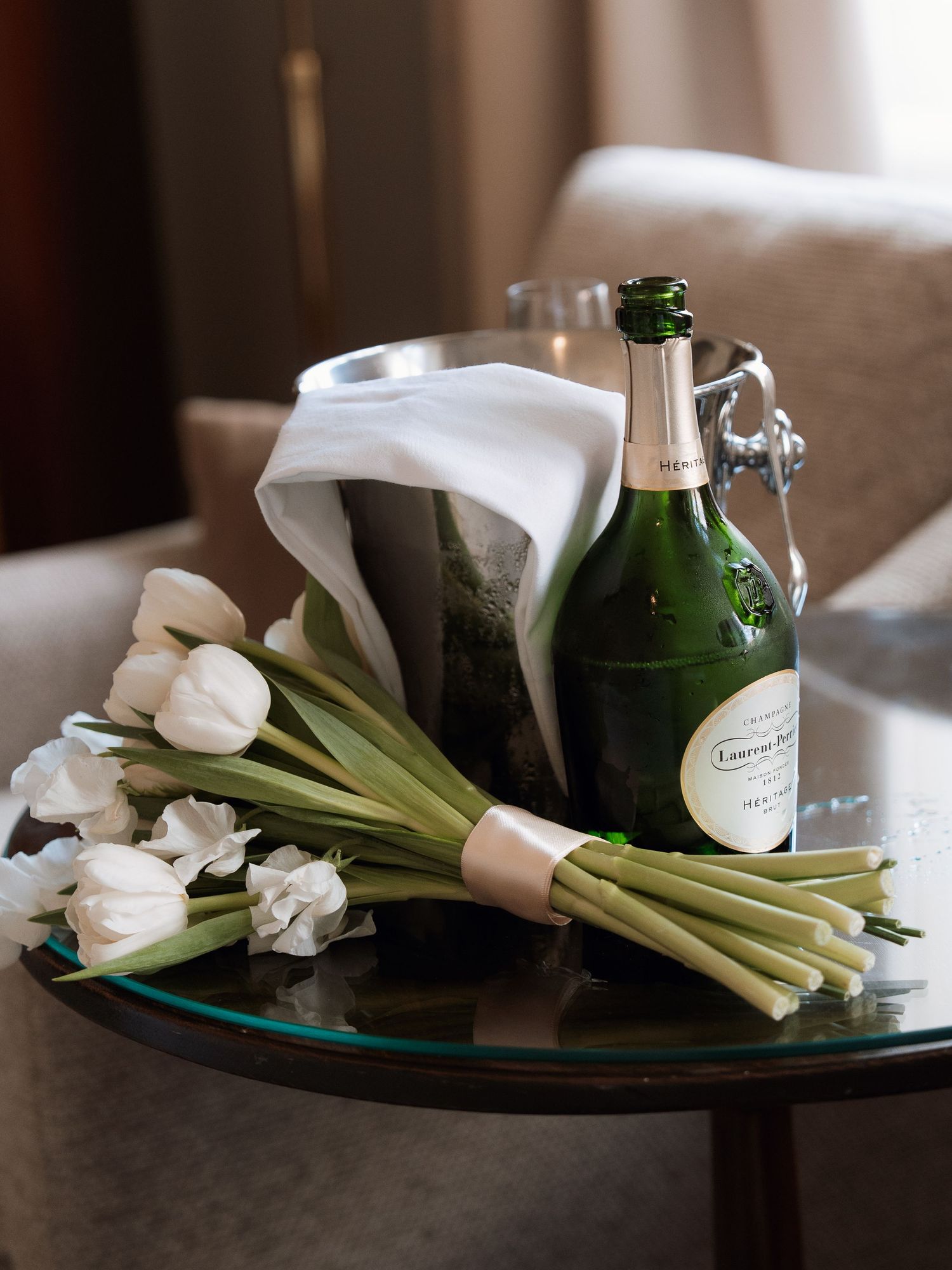 White calla lilies and green glass bottles create an elegant still life composition on a dark surface.