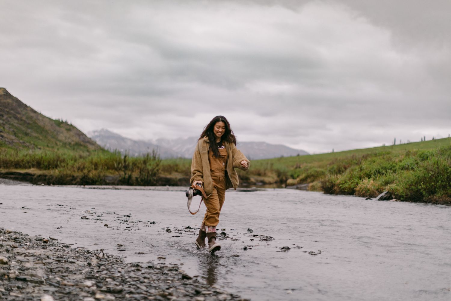 Alaska wedding photographer walking through a river with camera in Denali National Park.