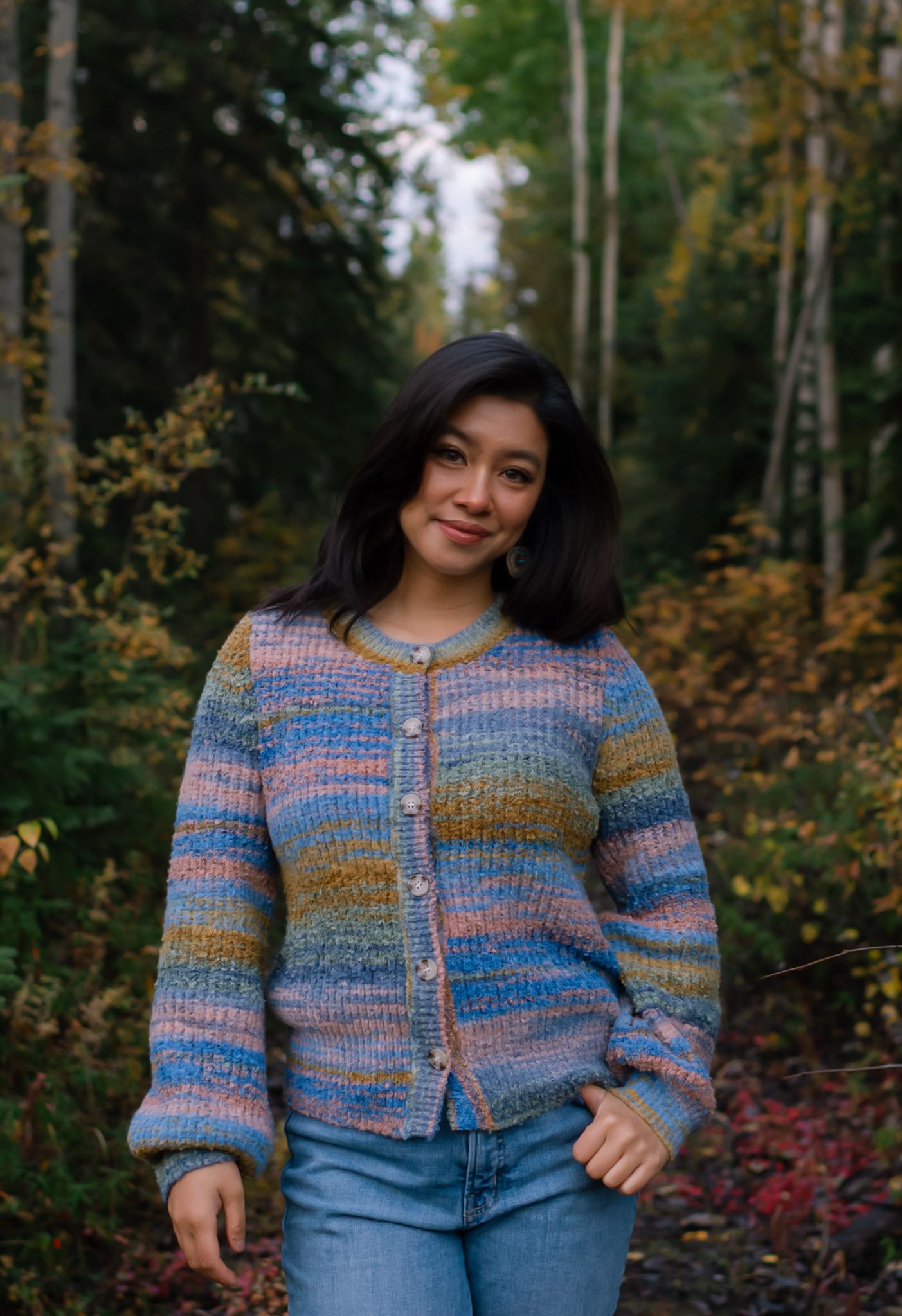 Lifestyle portrait photographer self-portrait in an autumn forest wearing a colorful knitted cardigan.