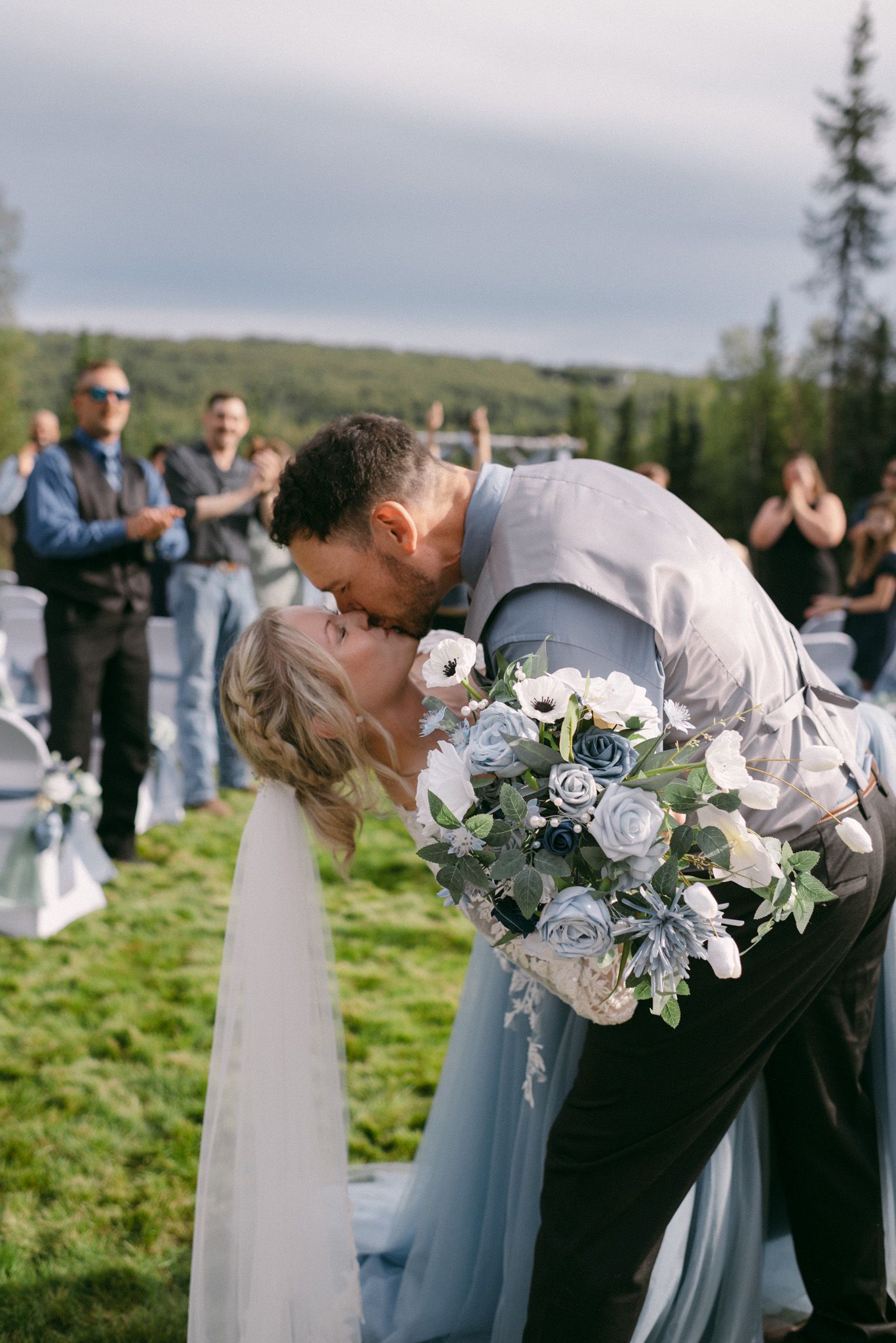 Couple sharing their first kiss in the backyard ceremony surrounded by loved ones in Fairbanks, Alaska.
