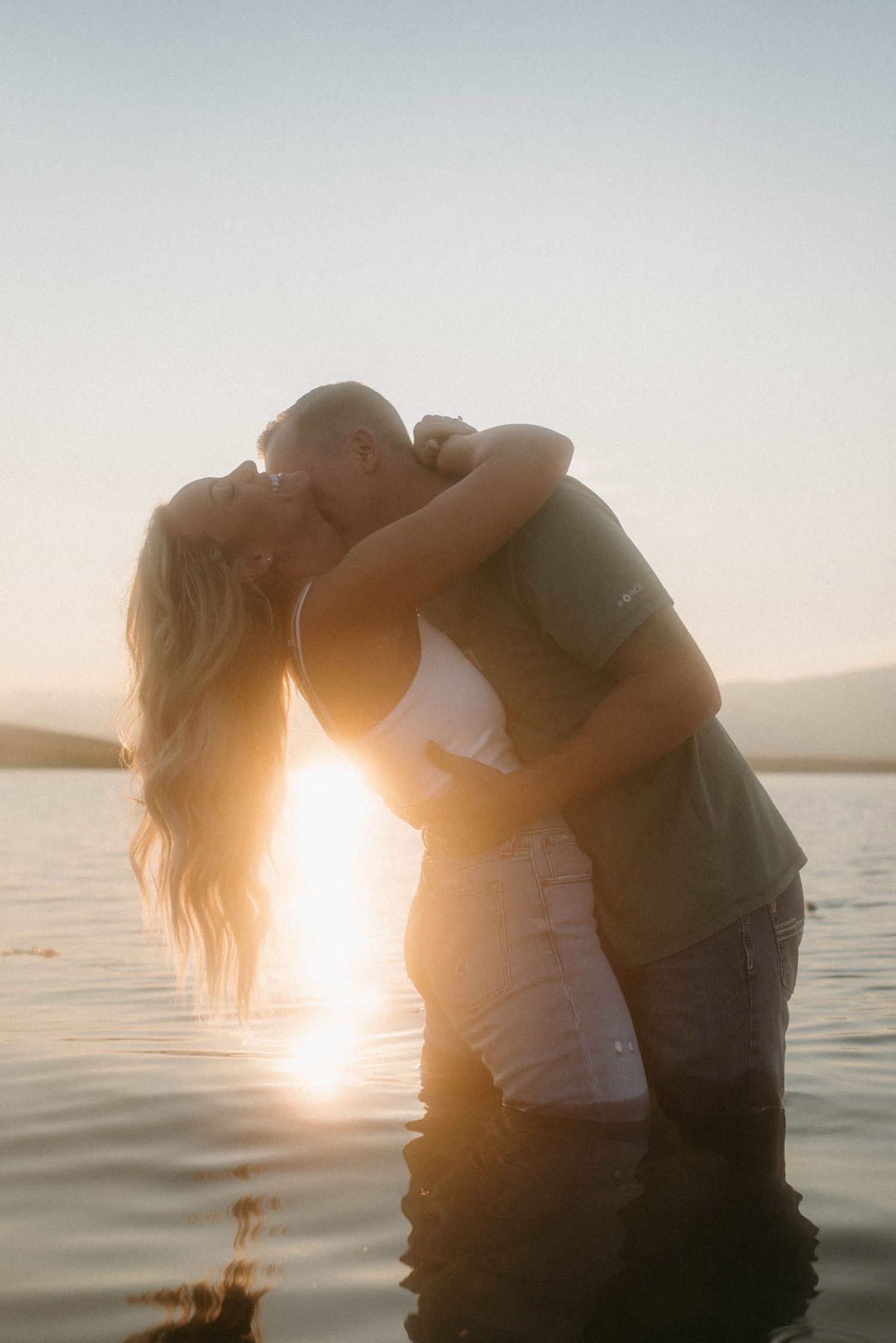 Romantic couple standing on lake with Montana landscape at sunset.