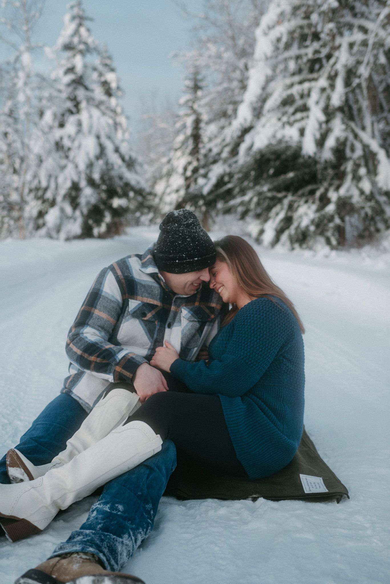 Engaged couple sitting on a blanket in a serene winter landscape, celebrating their engagement in the solitude of Fairbanks, Alaska.