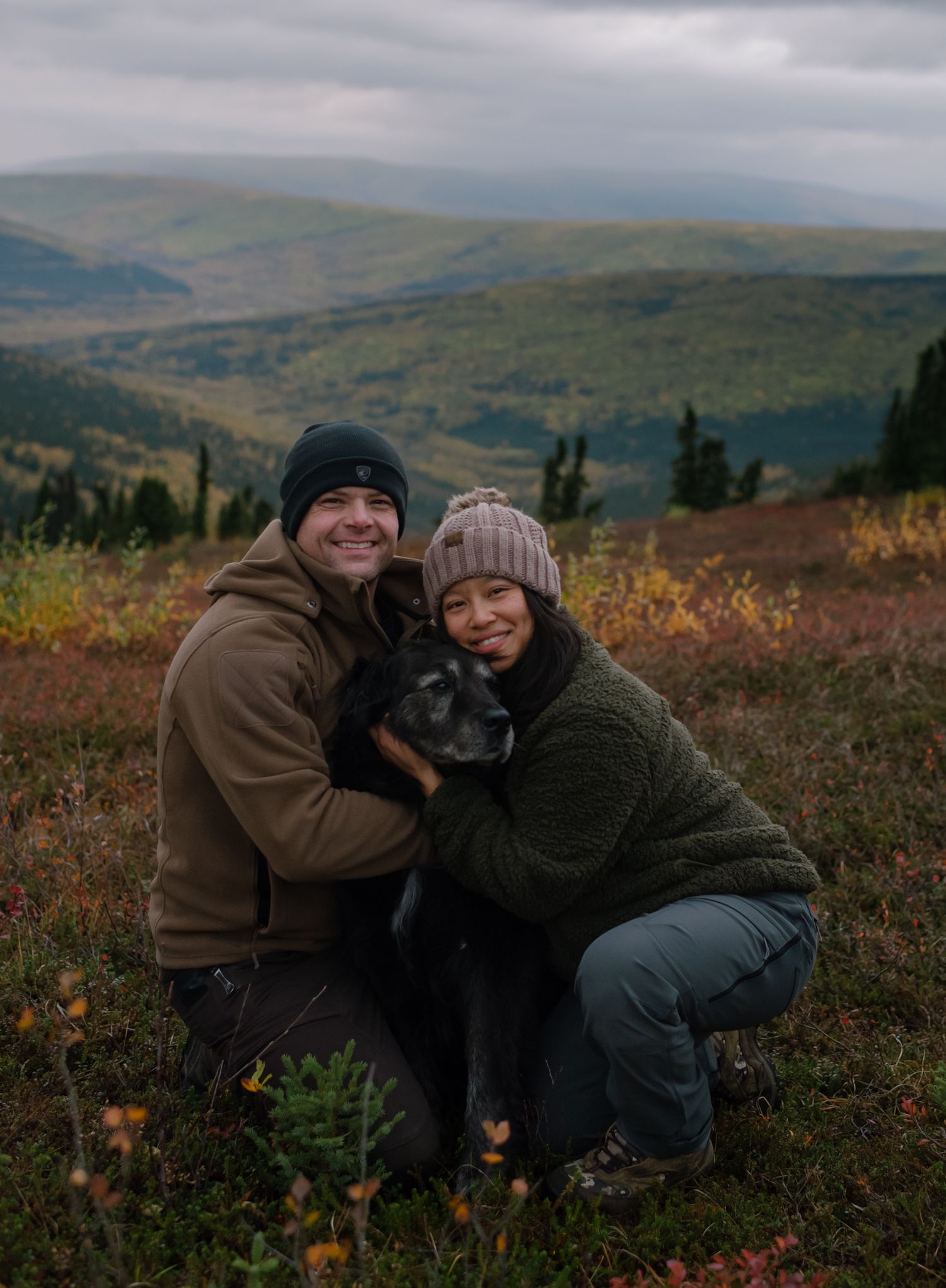 Natural family photography session in the Alaska mountains featuring a couple and their dog surrounded by colorful autumn landscape.