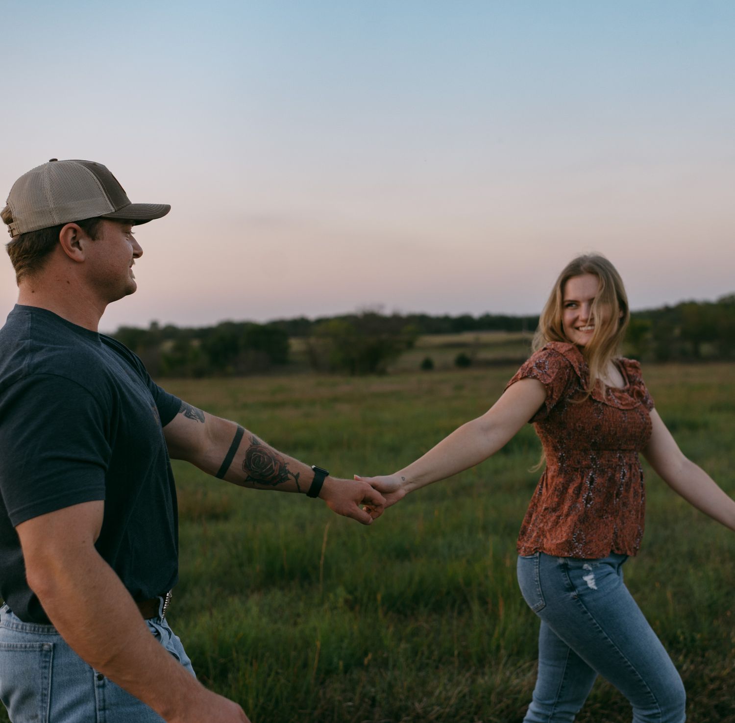 Couple walking through lush green fields during their engagement session in Kansas, celebrating their love together.