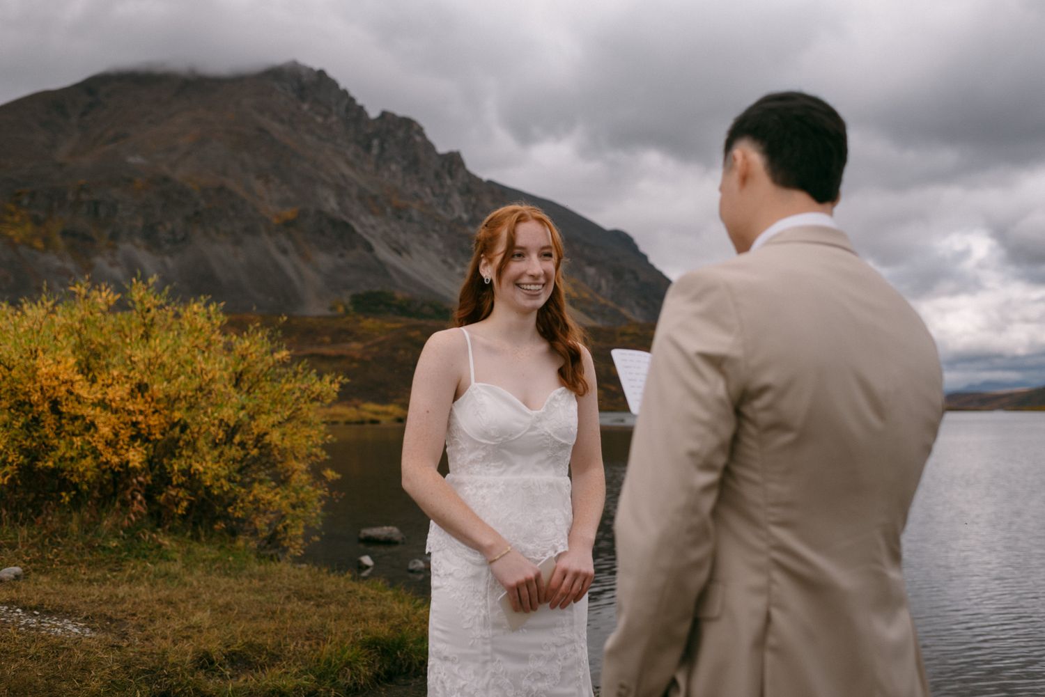 Bride and groom sharing their wedding vows as the bride smiles, surrounded by the mountains of Denali National Park, Alaska.
