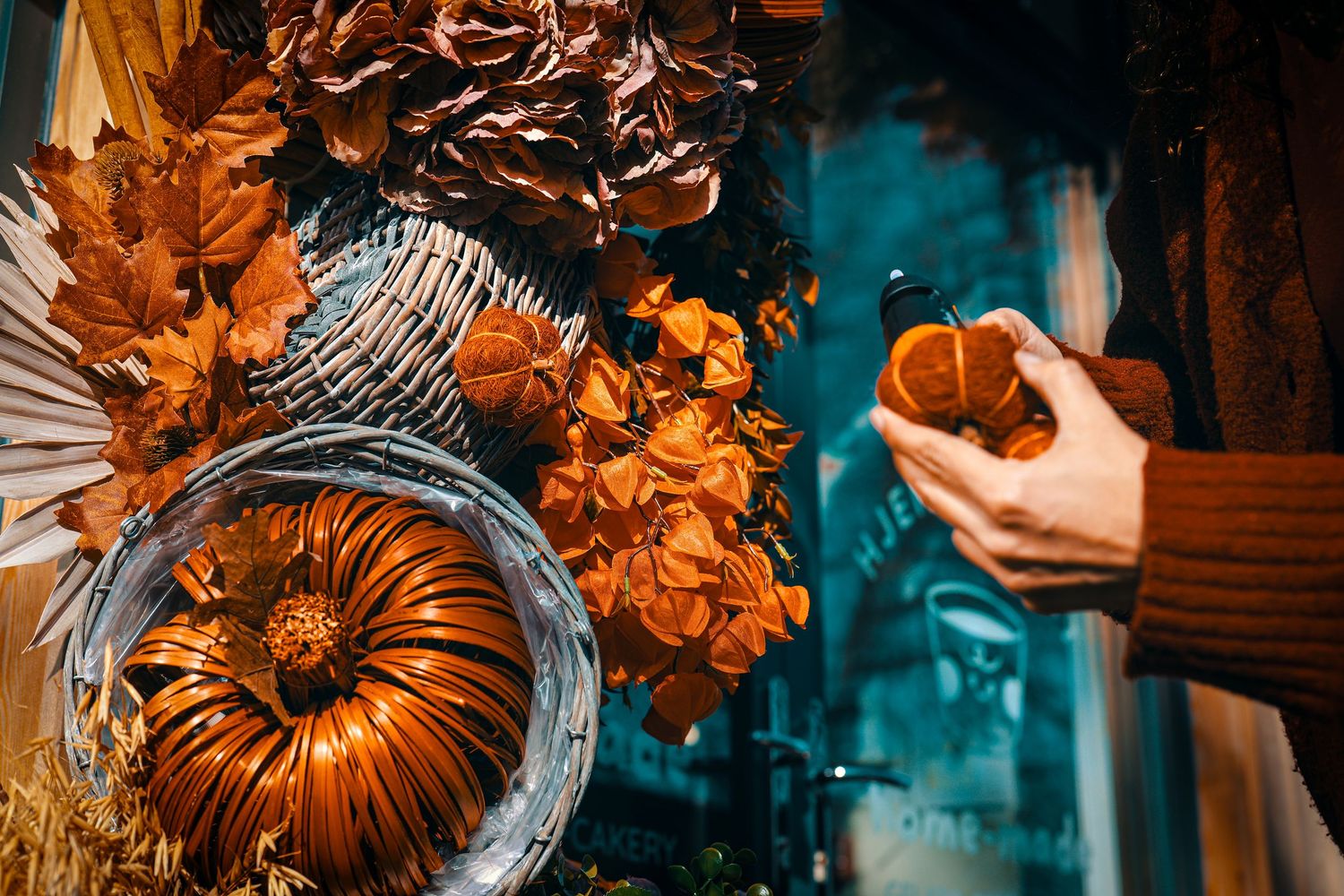 A metallic pumpkin decoration and autumn leaves against a teal background with a hand holding a small object.