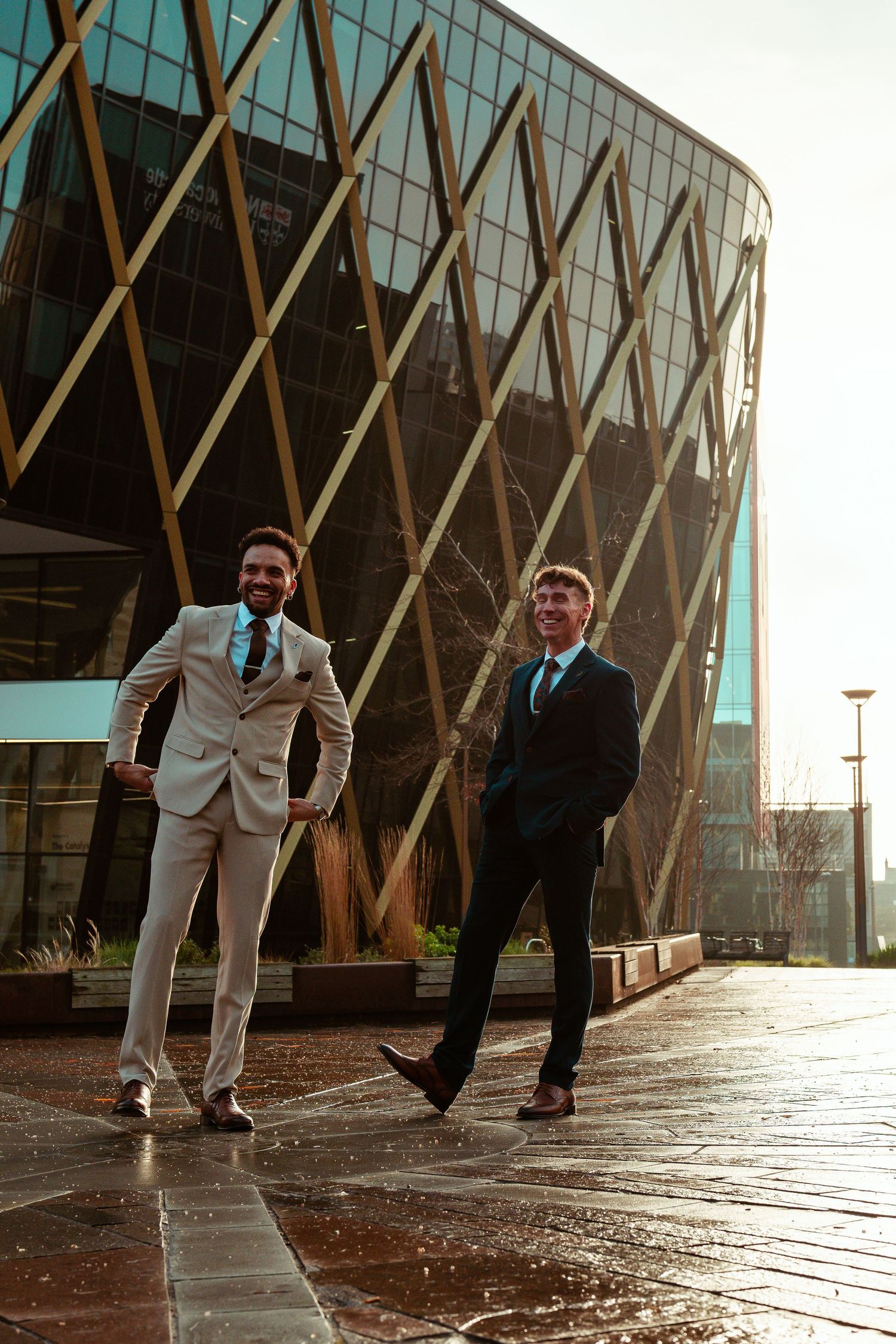 Business professionals in suits stand outside a modern glass building with diagonal architectural features on a wet day.