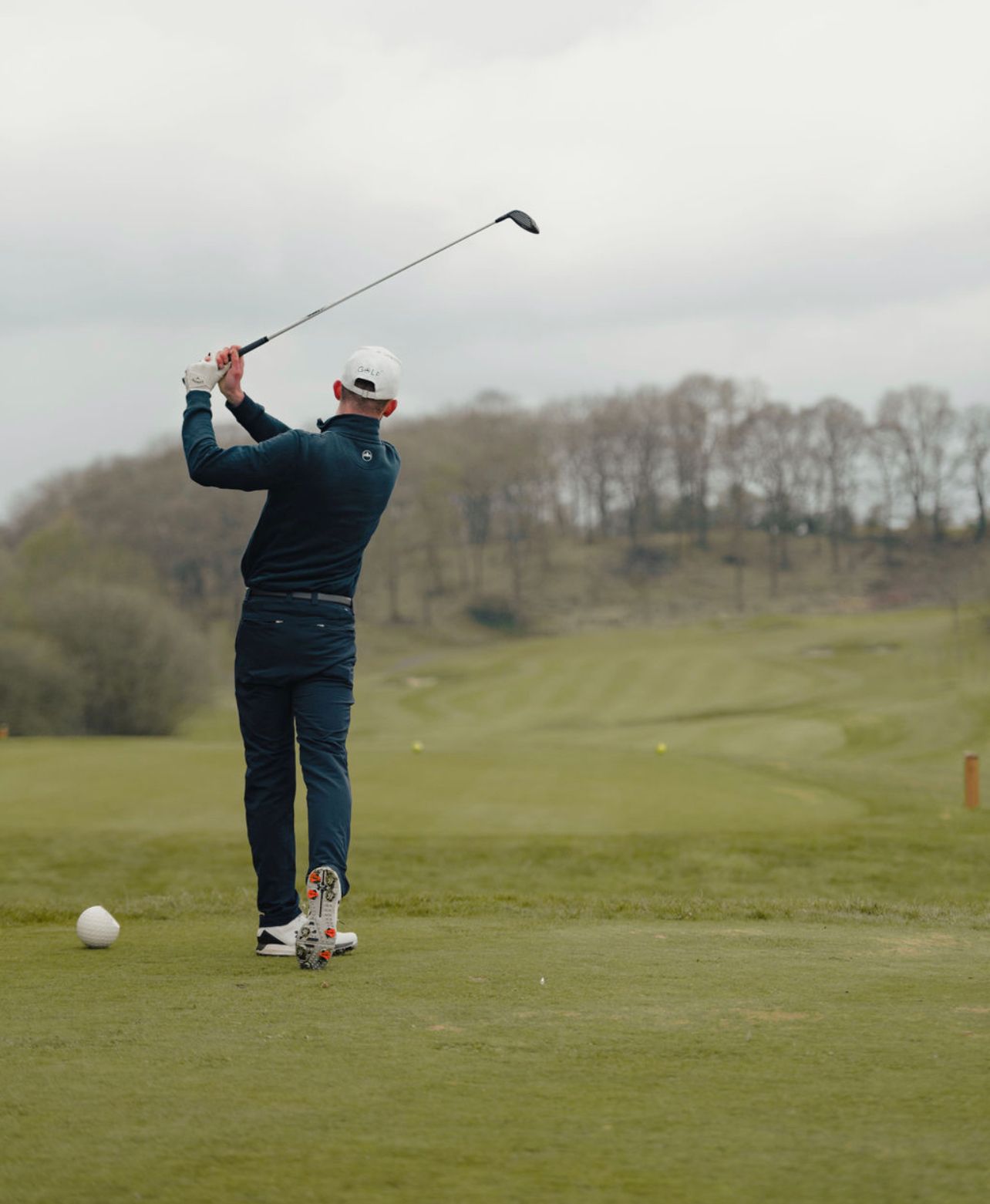 A golfer follows through on their swing while practicing on a lush green course with trees in the background.