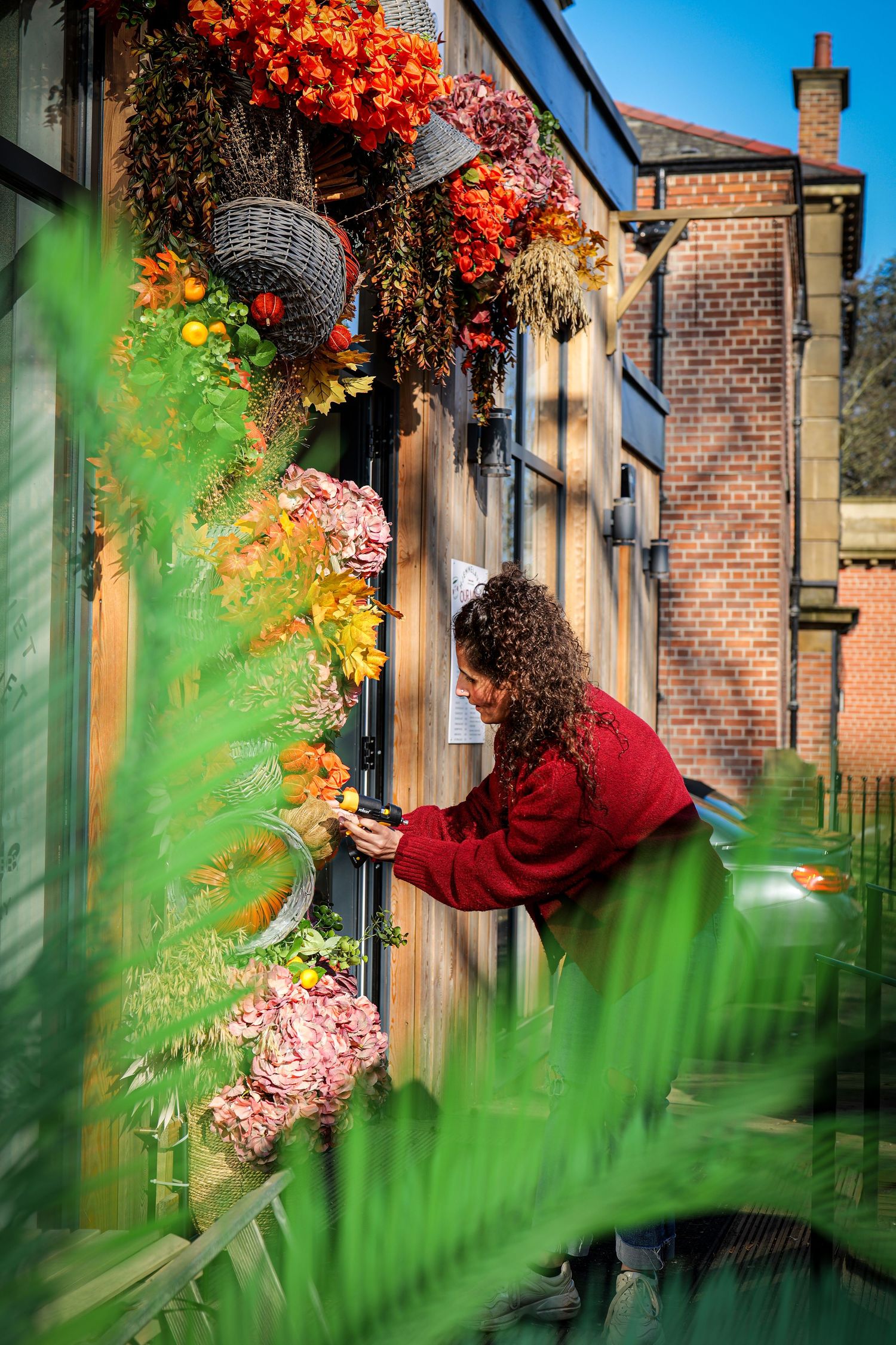 Artistic sequence of red autumn leaves against brick building with green foliage blurred in foreground.