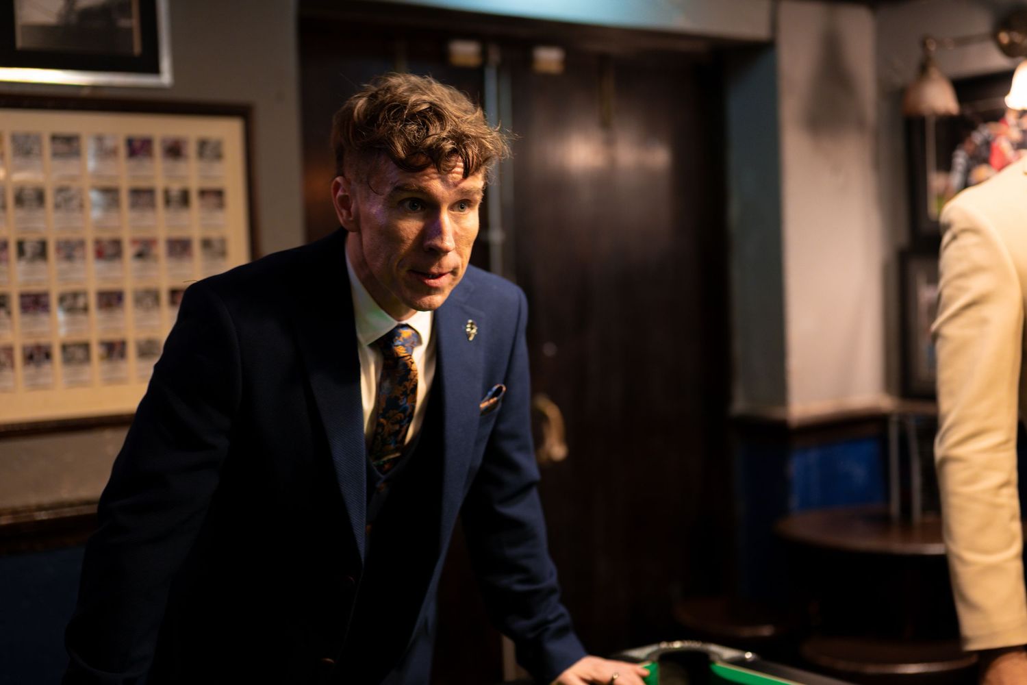 A person plays snooker in a dimly lit room with framed photos on the wall.