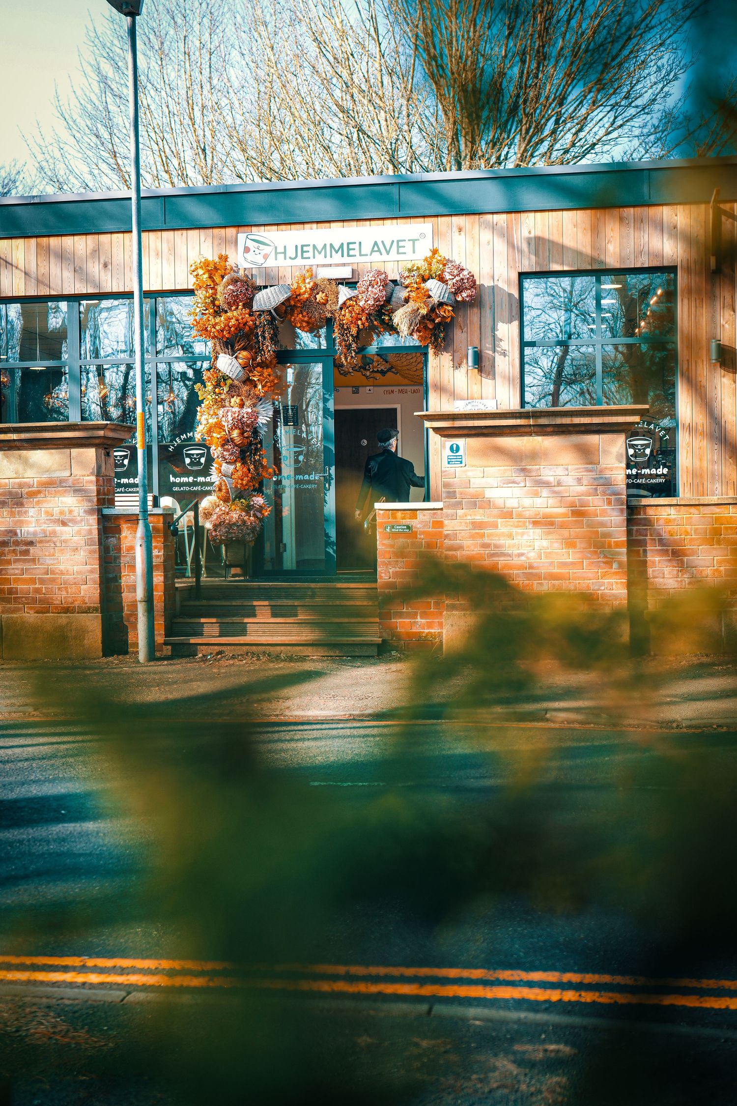 A brick building exterior with sunlit windows and autumn foliage casting shadows in warm afternoon light.
