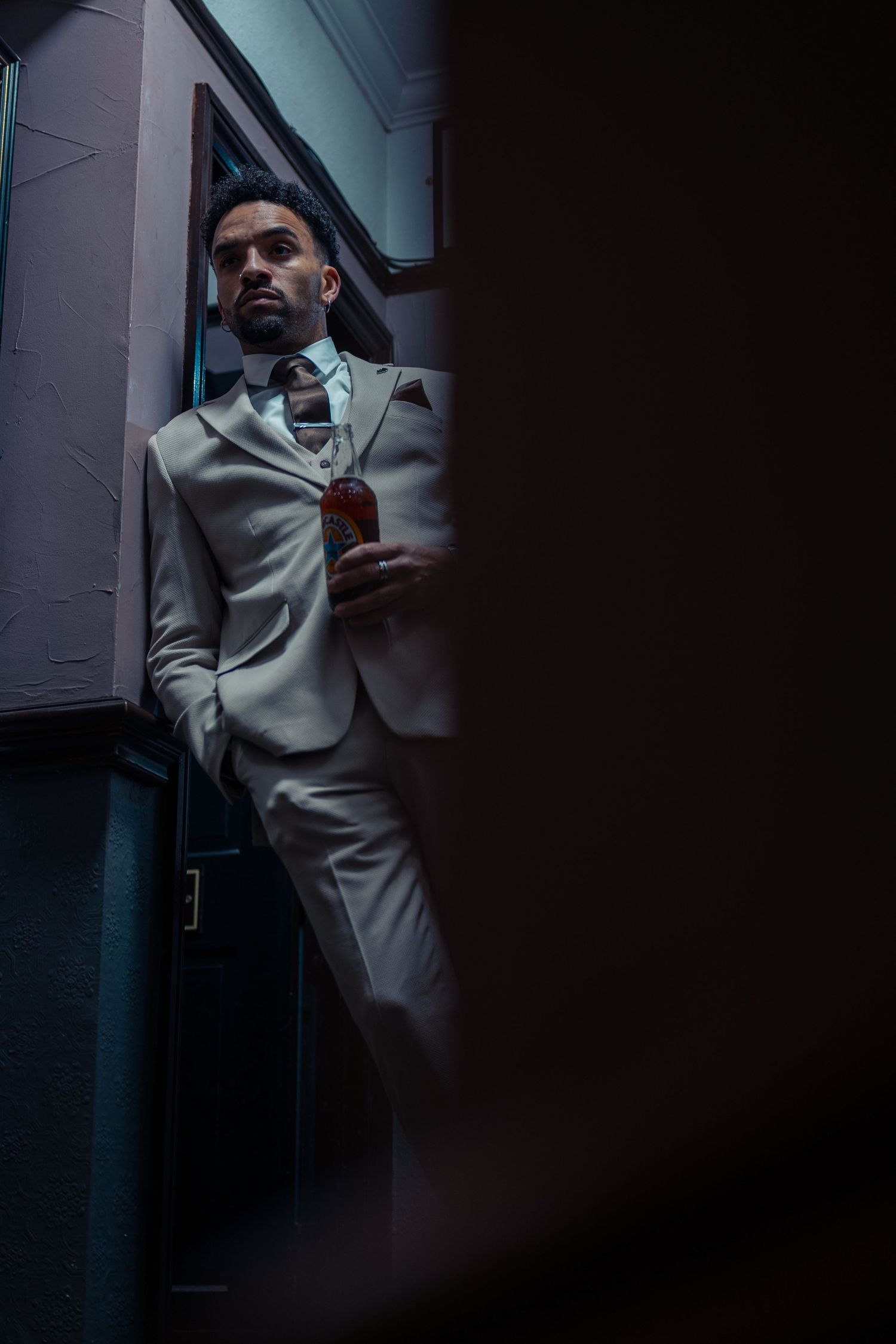 A person in a gray suit poses against a dark background in a dramatic moody lighting setup.