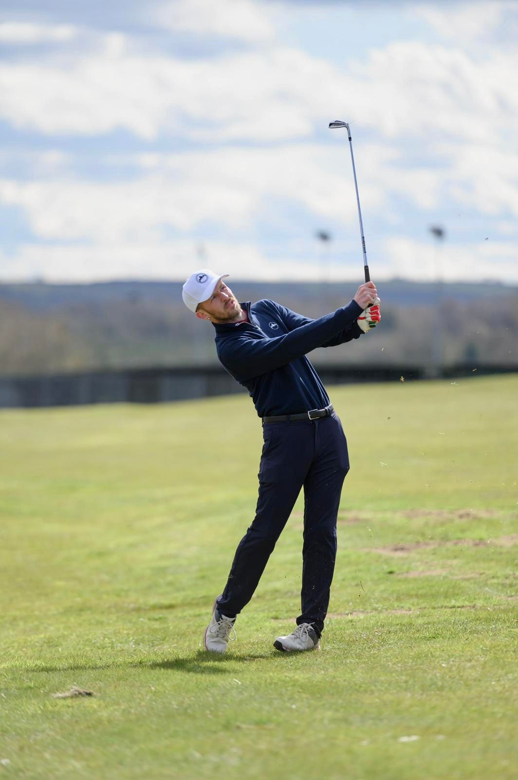 A golfer in navy blue attire demonstrates an exaggerated follow-through swing sequence on a grassy course.
