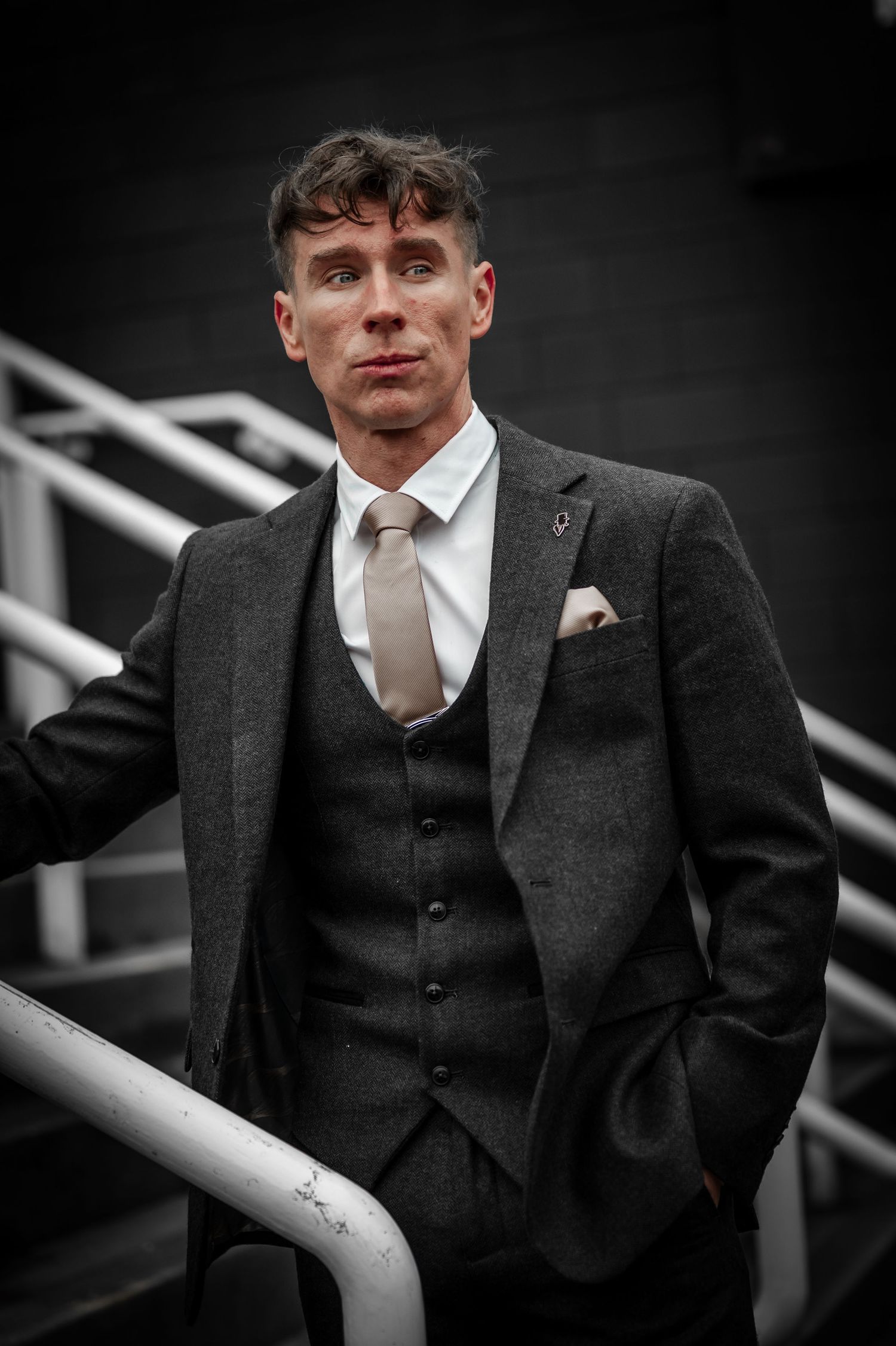 A person in a vintage-style three-piece tweed suit and white tie poses against a dramatic black and white background.