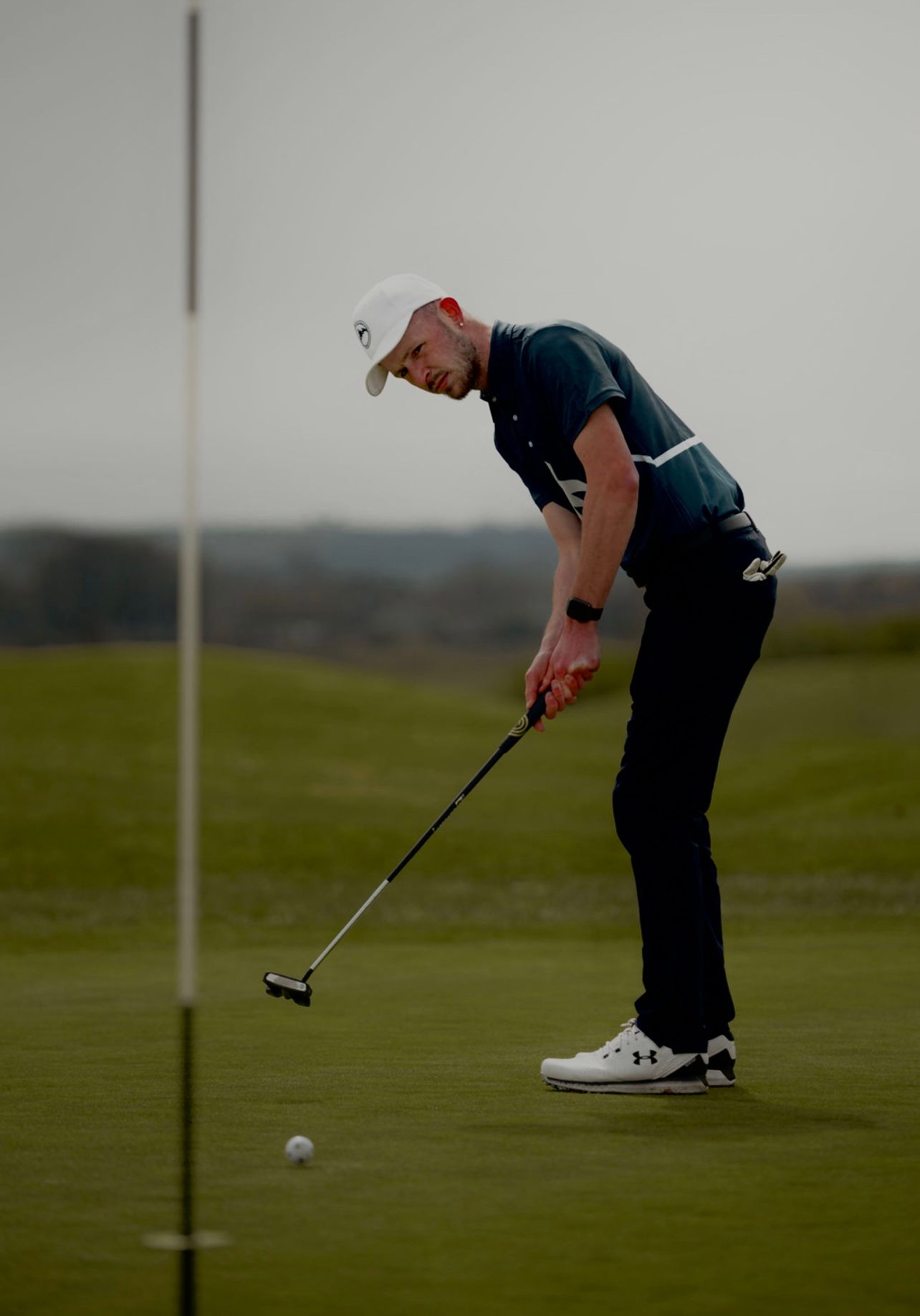 Golfer lines up and executes a putting stroke on a green golf course during overcast conditions.