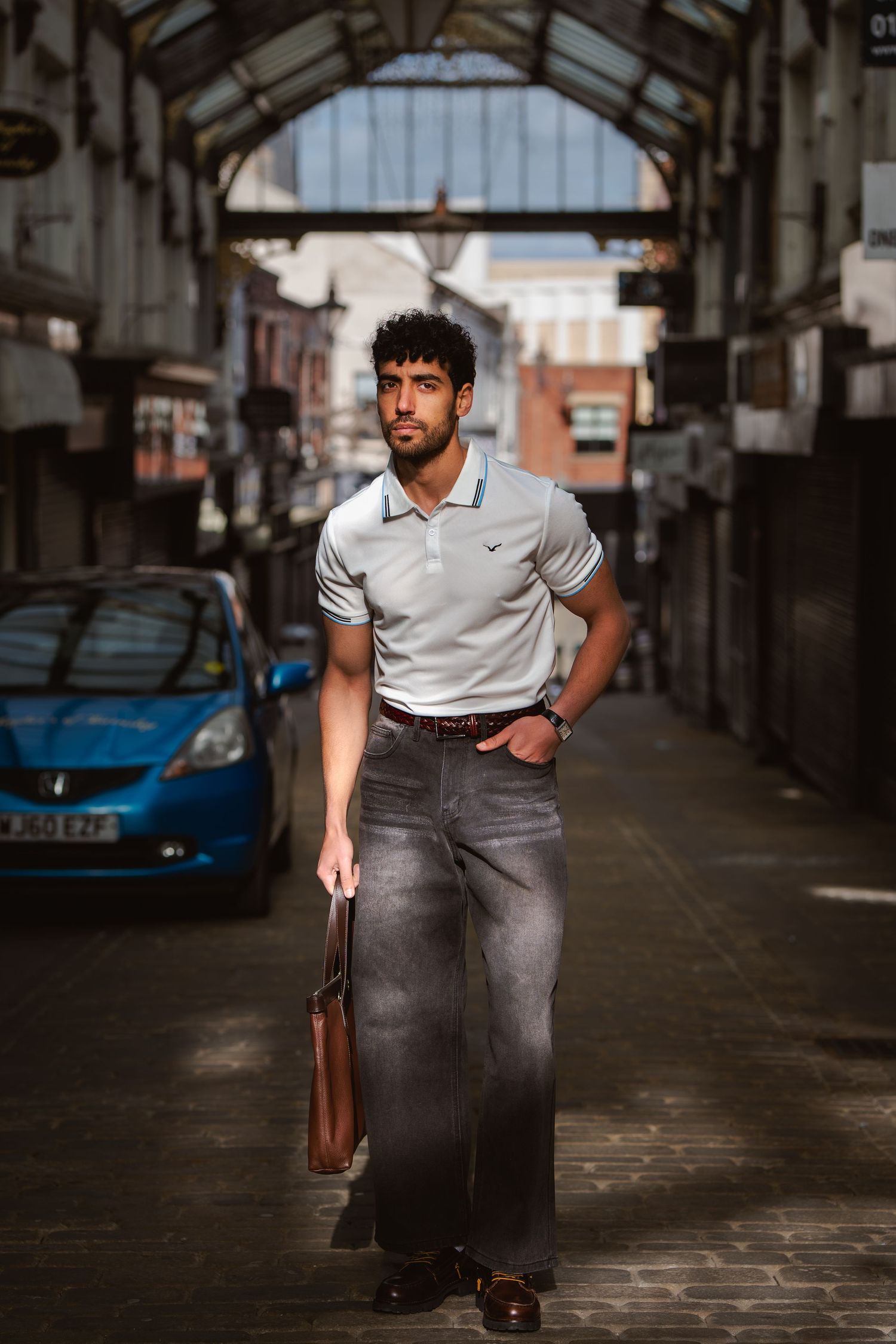 Stylish man in white Nike polo and grey wide-leg jeans walking through covered market passage.