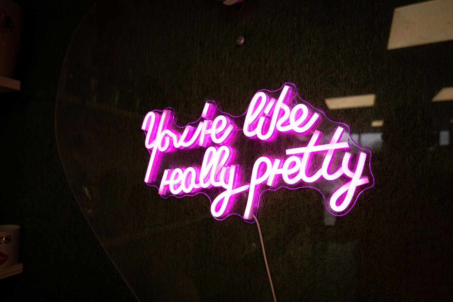 A pink neon sign mounted on a dark wall displays cursive text that reads 'really pretty'.