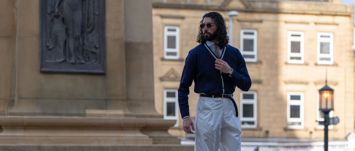 Stylish man with long hair wearing navy shirt and white trousers standing outdoors near a classical monument.