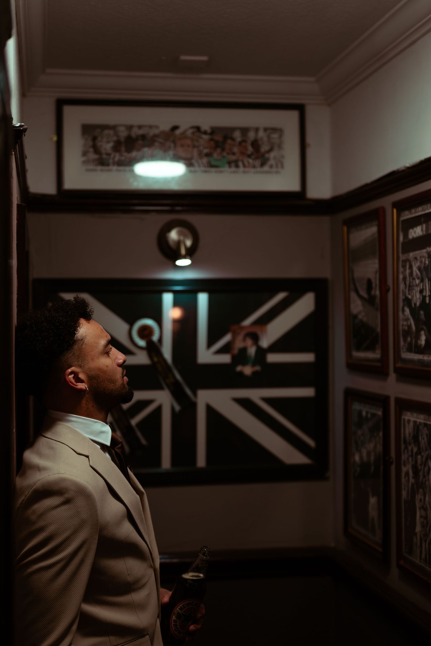 A series of dark moody photographs showing a figure in a beige suit standing in a dimly lit hallway with framed artwork.
