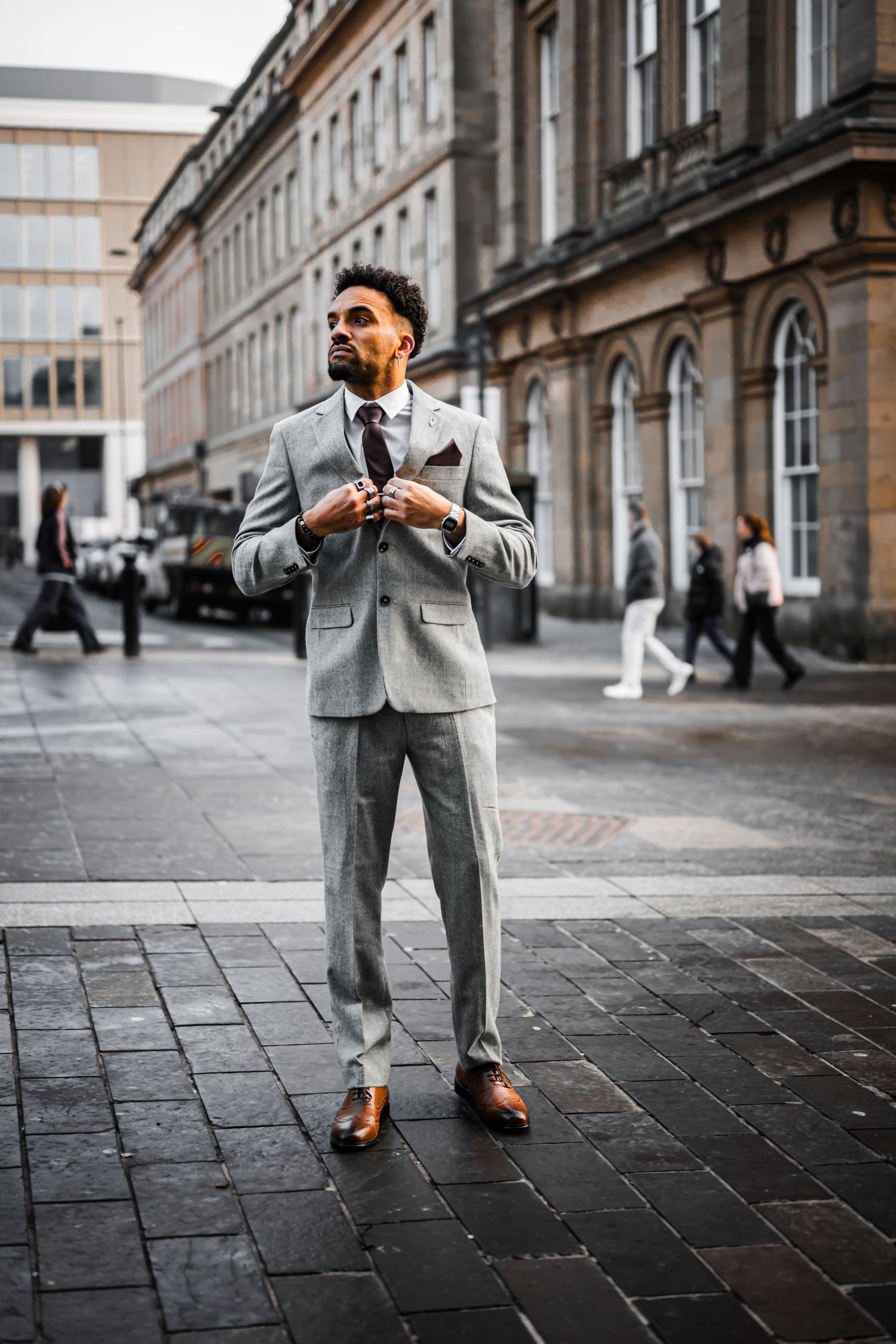 A person in a stylish gray suit strikes different poses on a cobblestone street in front of historic buildings.