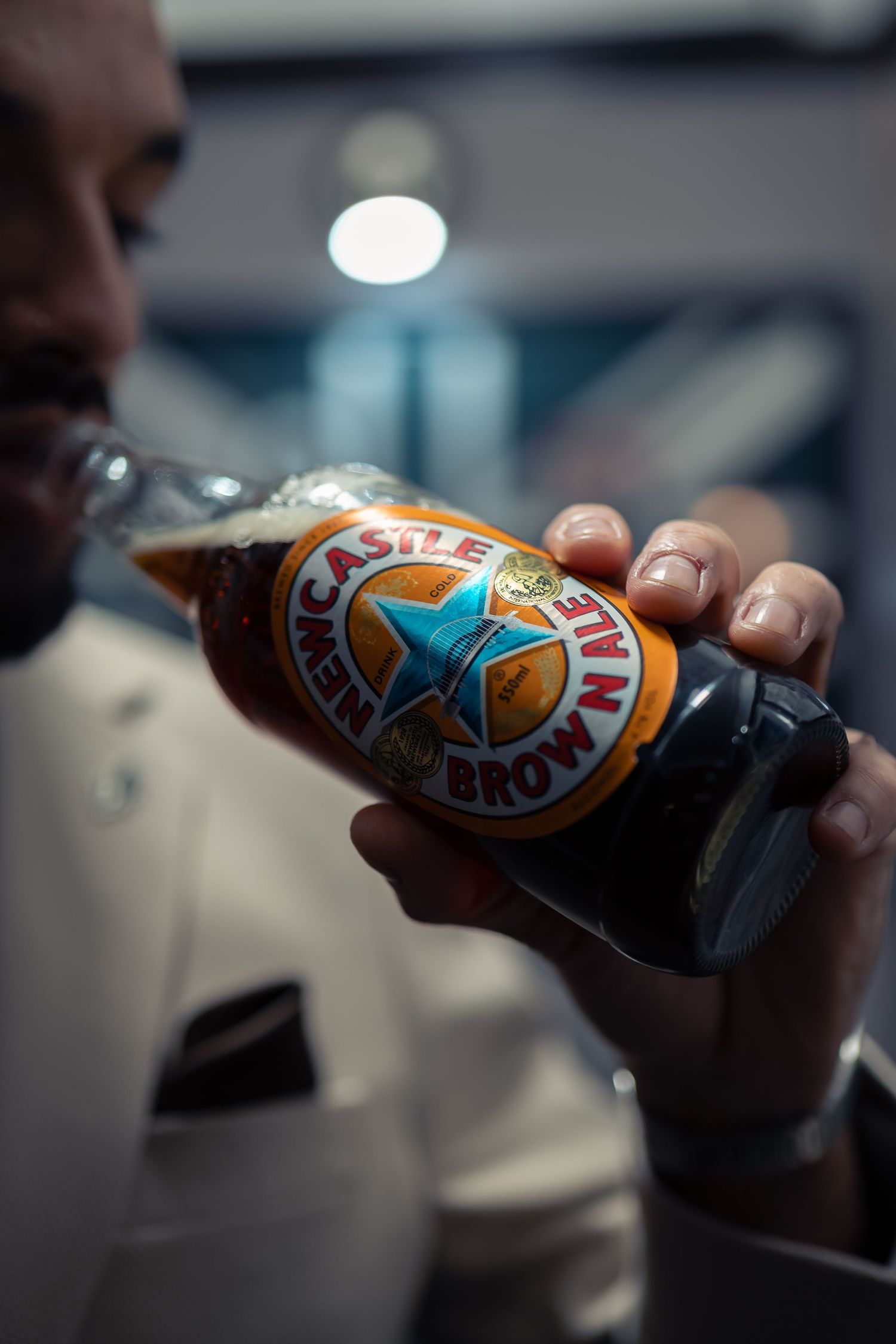 Someone holds a bottle of Newcastle Brown Ale beer in a dimly lit setting, showing the distinctive blue star logo.