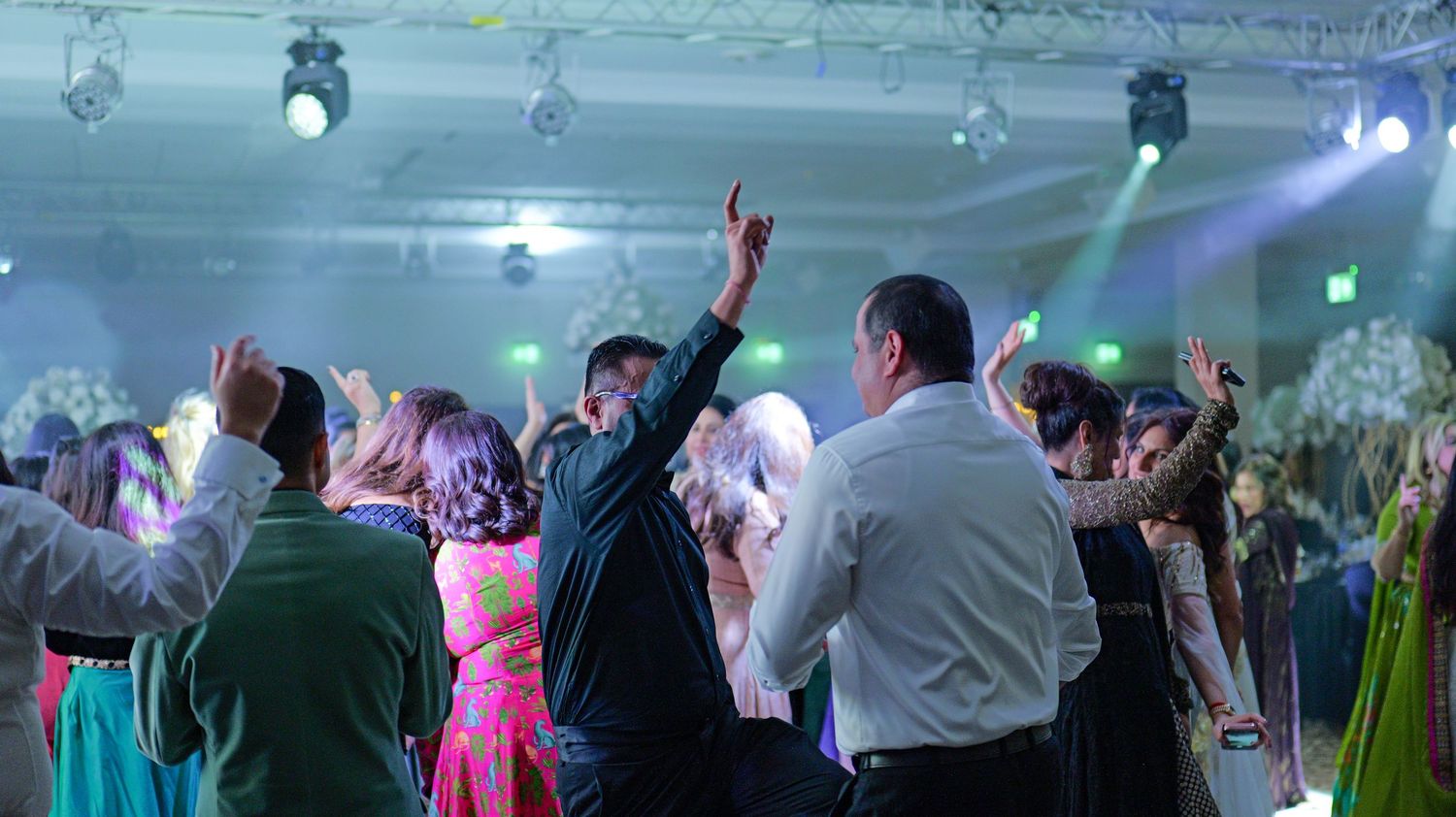 Crowd of party guests dancing under colorful spotlights at an elegant wedding reception with festive atmosphere.