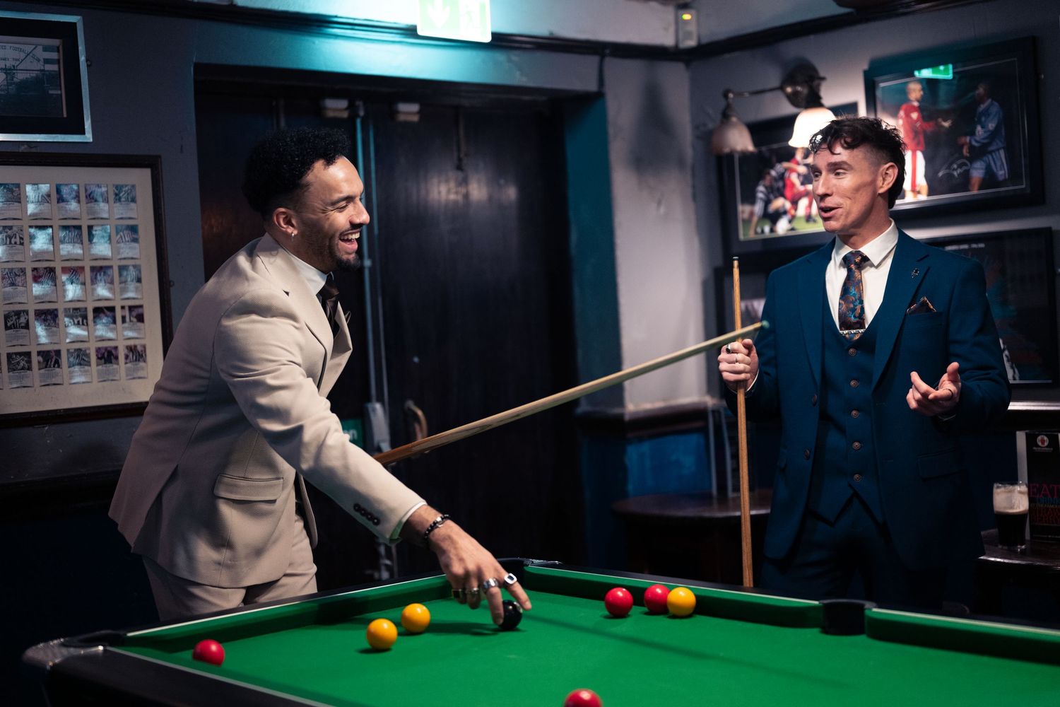 Professional snooker players compete on a dark-lit table with colored balls during an intense tournament match.
