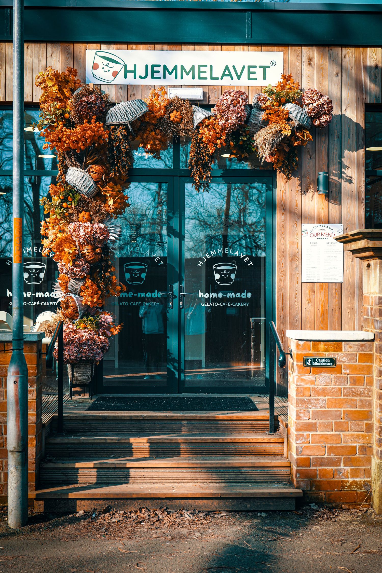 Rustic wooden storefront of Hjemmelavet cafe with orange autumn flowers decorating the entrance.