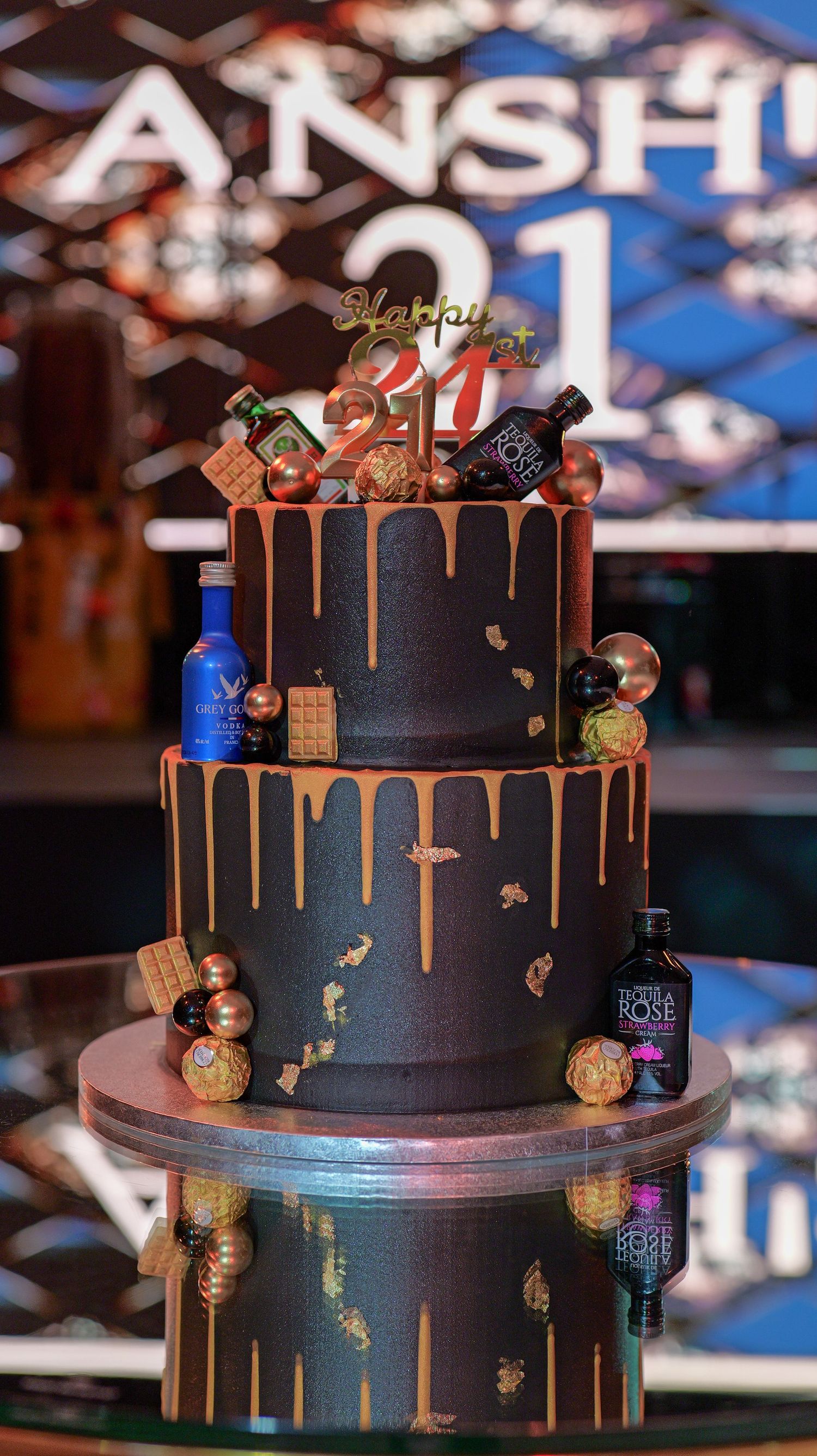 A black two-tier cake decorated with copper-colored drips and small Halloween-themed decorative elements around the sides.