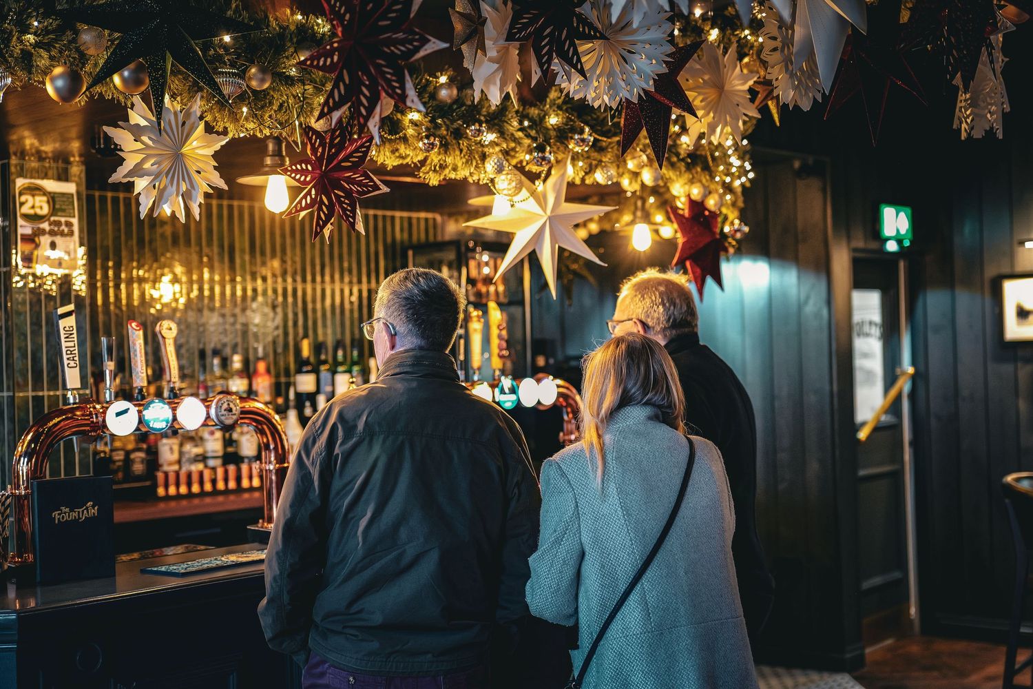 A dimly lit bar interior with decorative hanging lights and palm leaf decor creates a tropical ambiance.