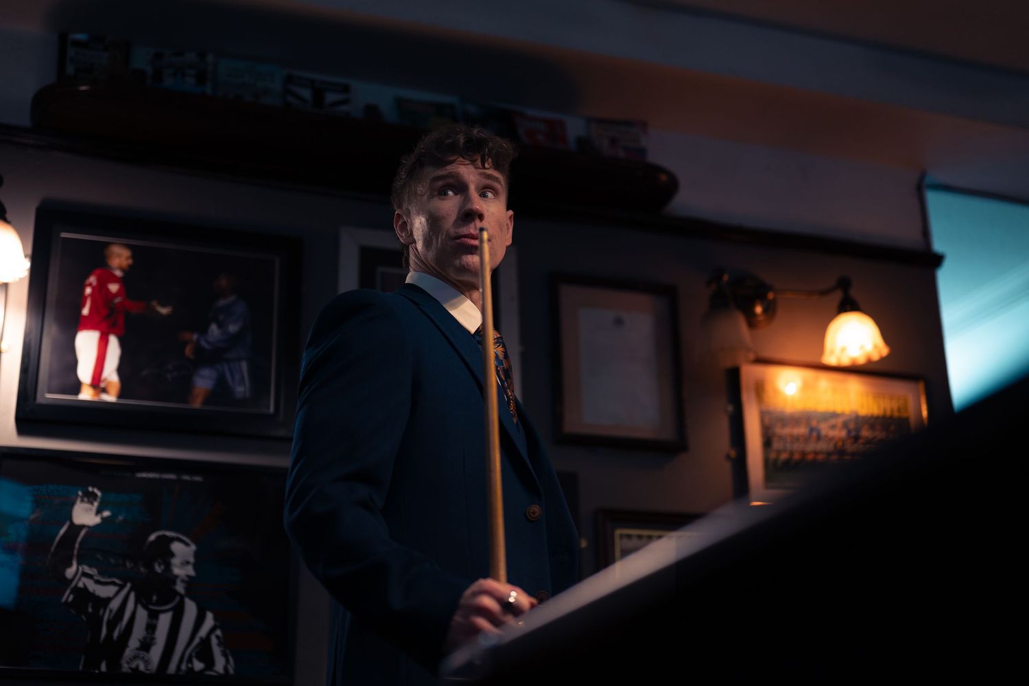 A person in a dark blue jacket stands in a dimly lit room with ambient lighting and wall decorations.