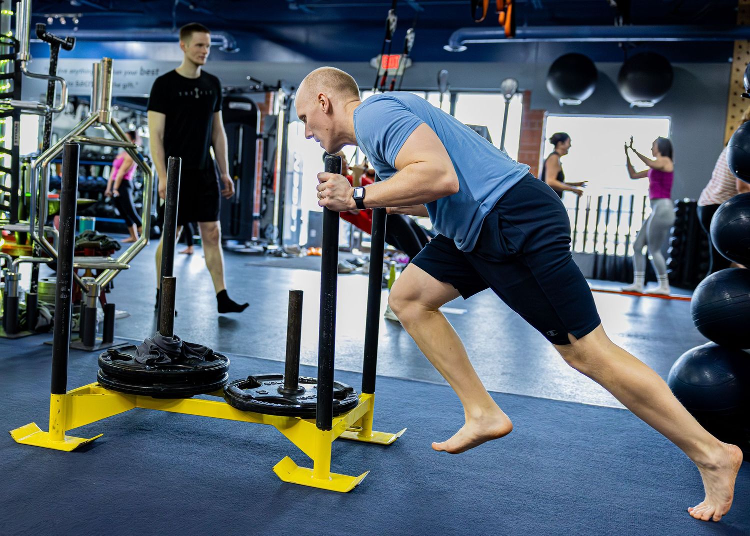 An athlete pushes a weighted sled barefoot during an intense gym training session.