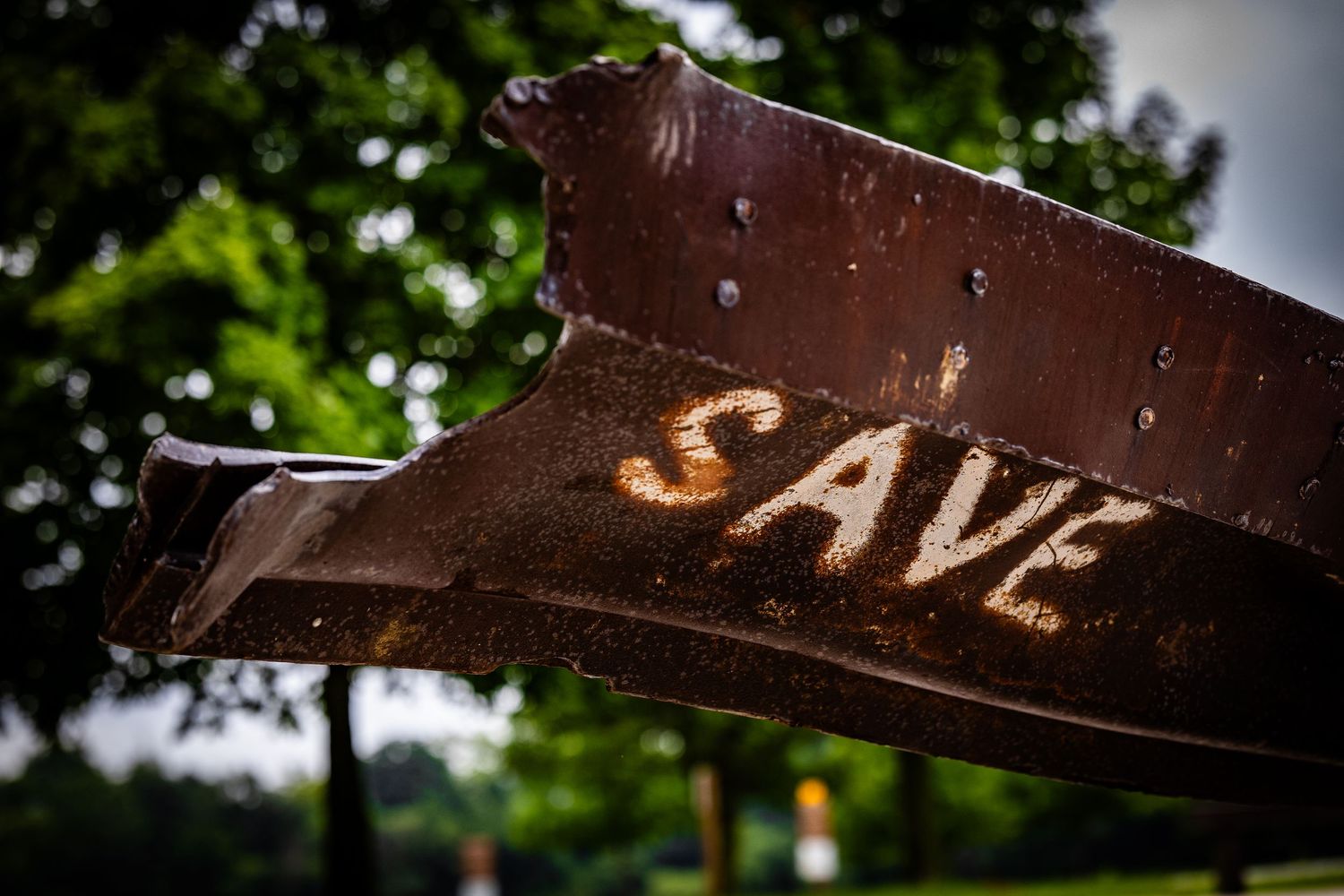 Rusty metal beam with the word SAVE painted in white letters outdoors.
