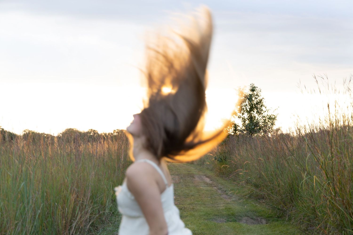 Woman flips dark hair dramatically in a field at sunset creating a motion blur effect.