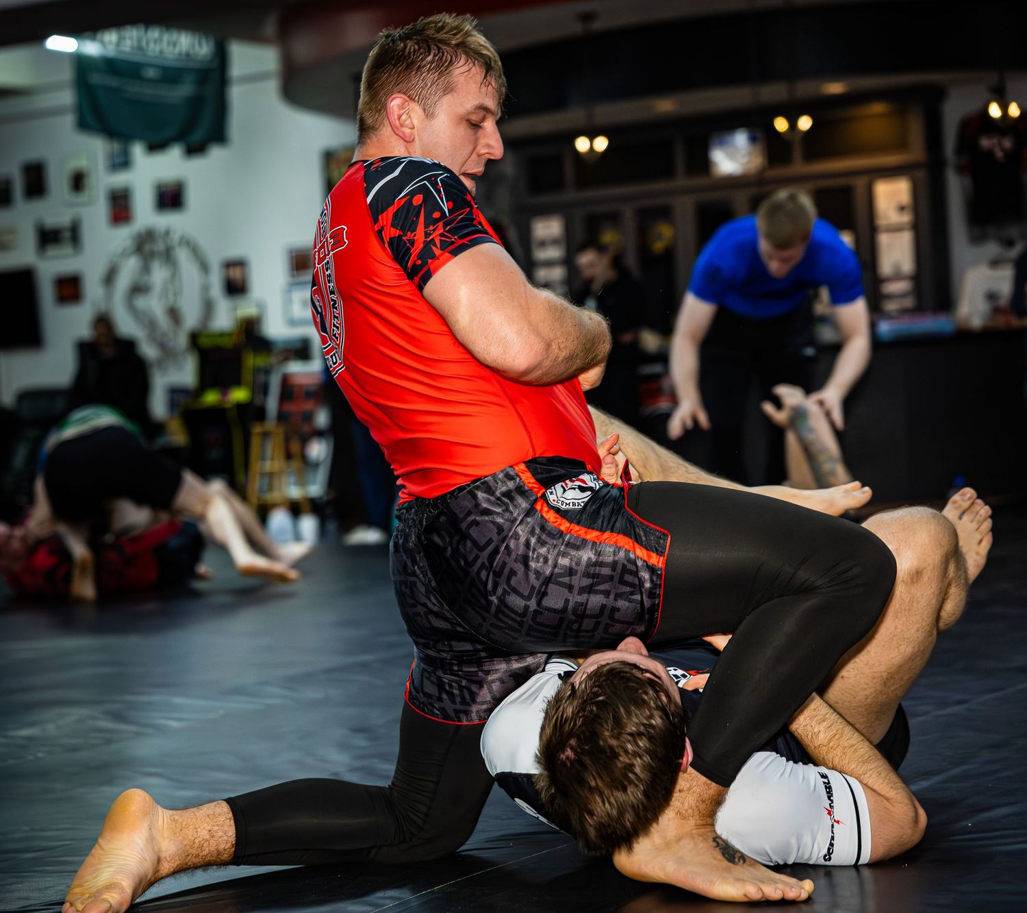 MMA athlete in red rash guard practices ground control techniques on a training partner.