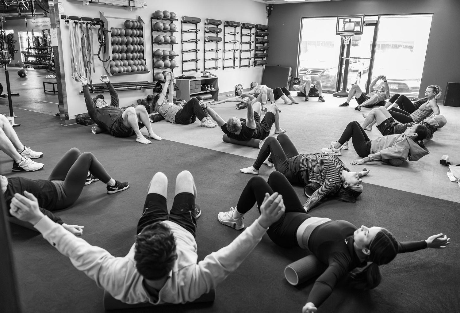 Group fitness class performing floor exercises on mats in a well-equipped gym.