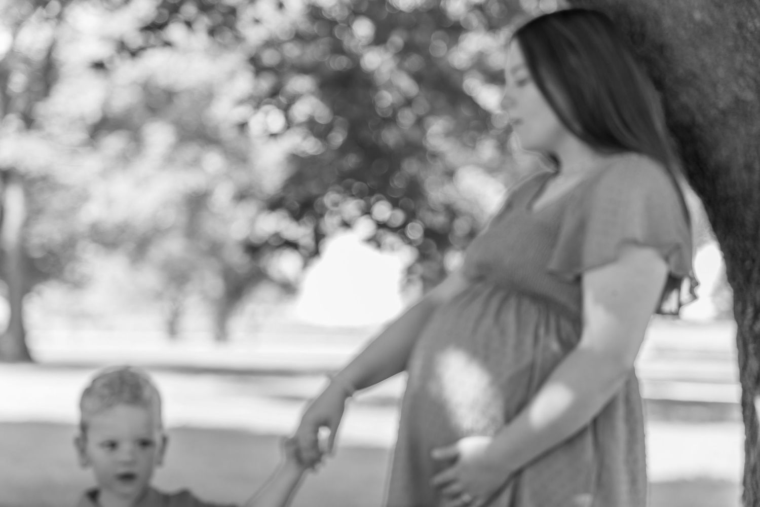 Black and white photo of a pregnant woman holding a child's hand in a park.